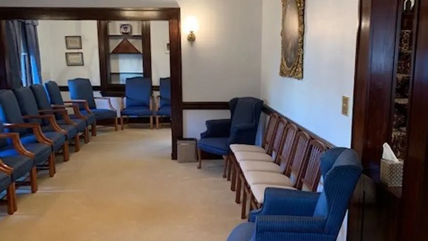 A quiet room with blue chairs, beige carpet, and a dark wood trim.