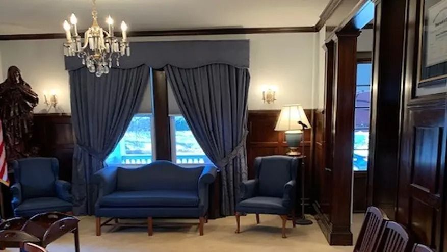 A formal room with blue furniture, curtains, and a chandelier. Dark wood paneling and a window.