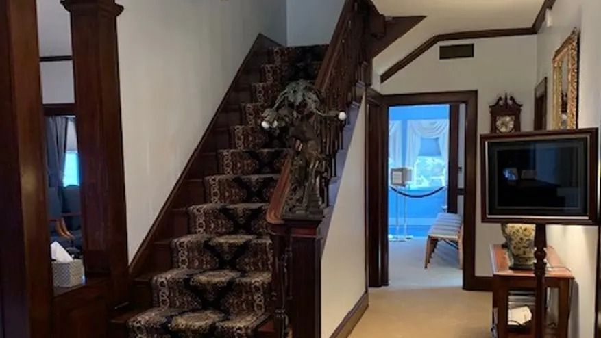 Interior hallway with wooden staircase and dark wood trim. A TV is mounted on a stand.