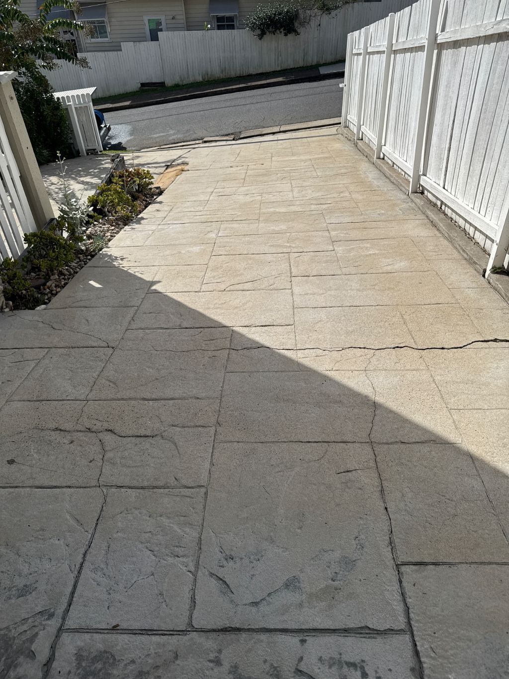 A concrete driveway leading to a house surrounded by trees and bushes.