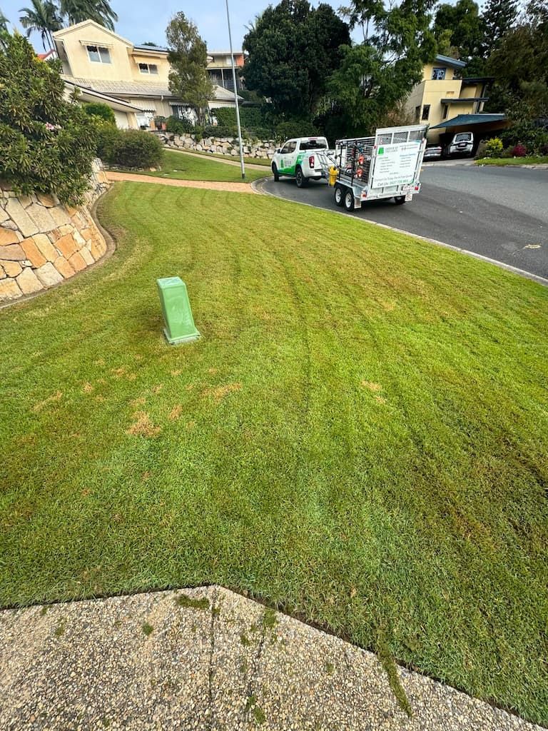 A lawn mower is cutting a lush green lawn next to a road.