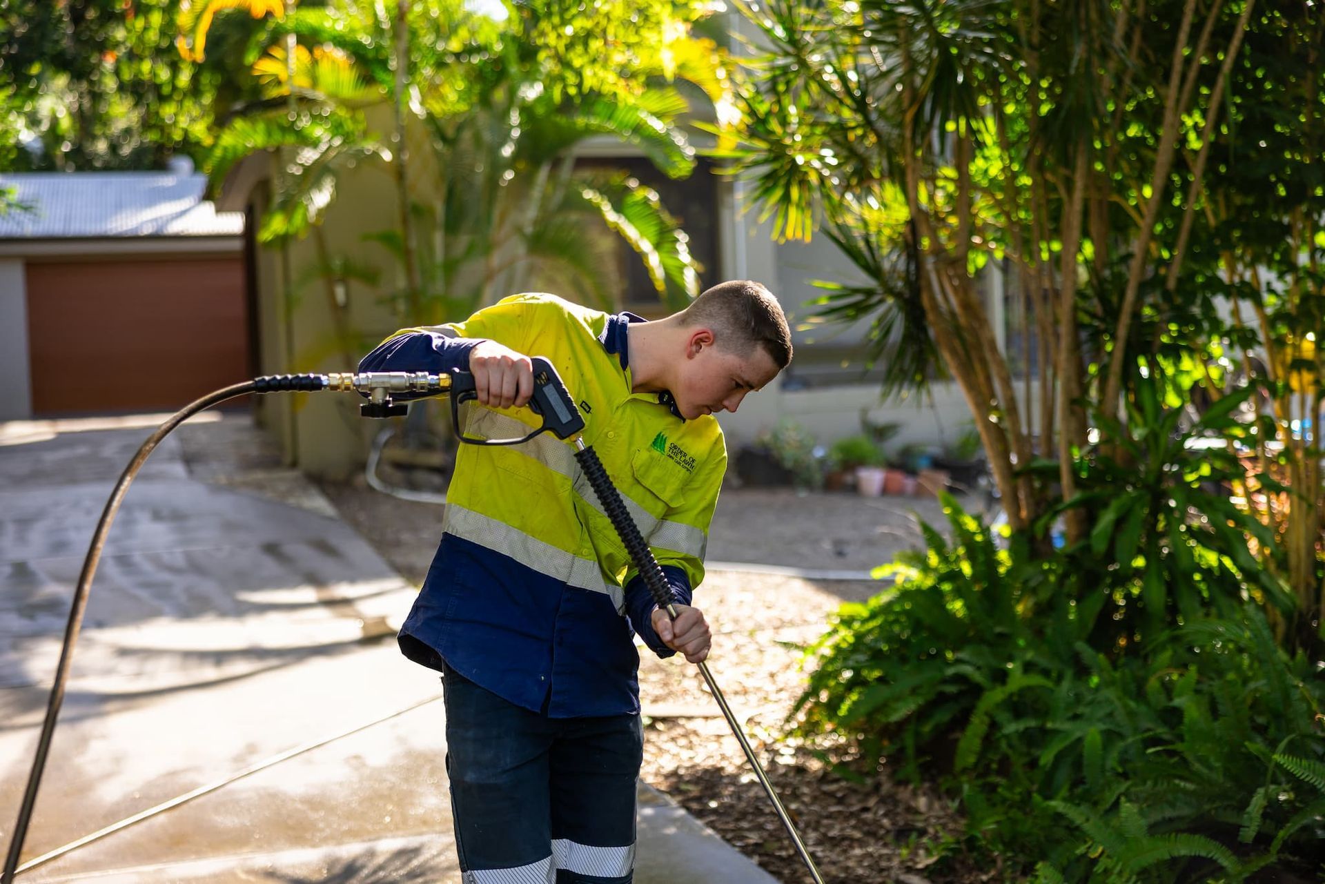 A man with a yellow shirt pressure washing a driveway