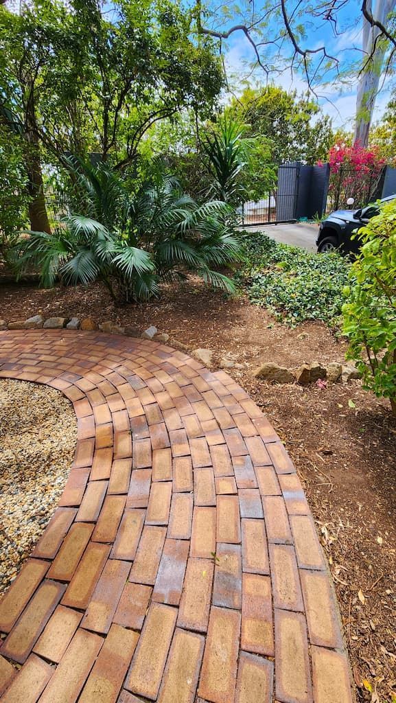 A brick walkway in a garden surrounded by trees and bushes.