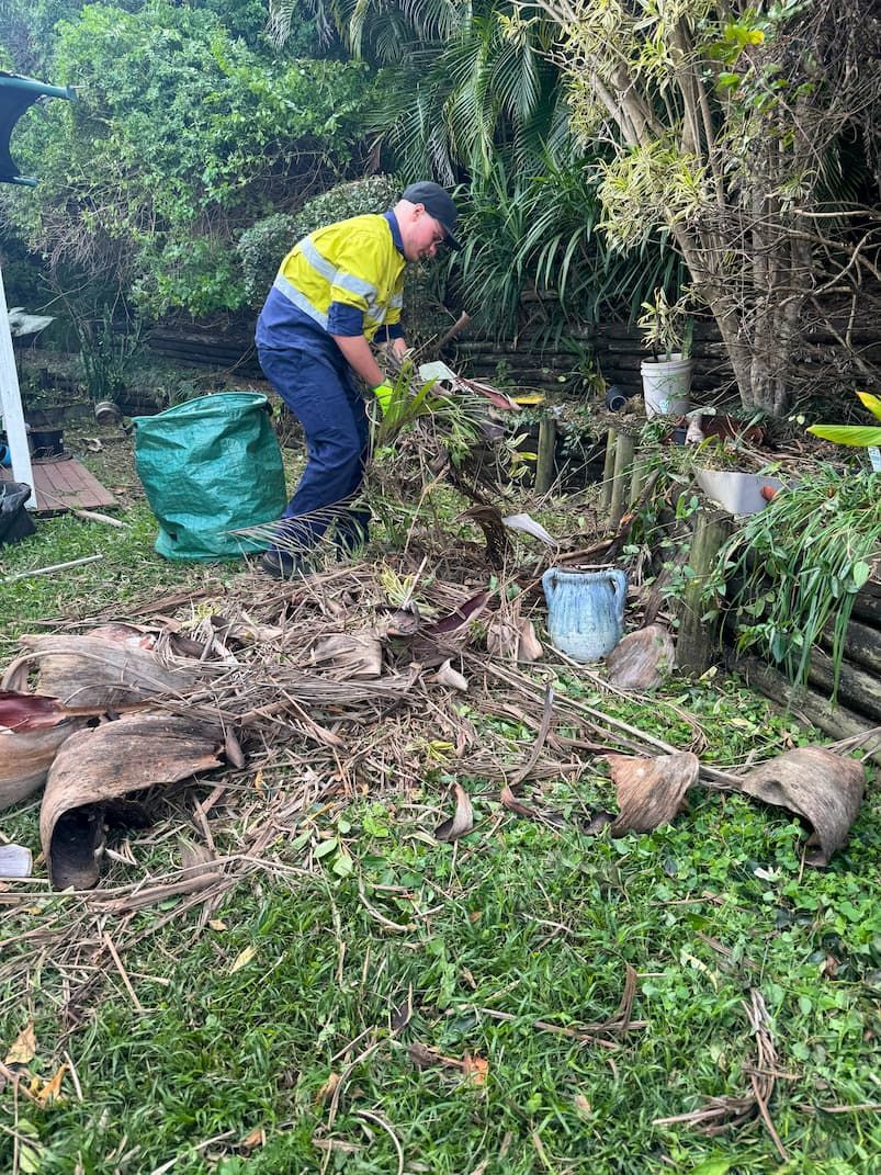A man is standing in a pile of green waste in a yard.