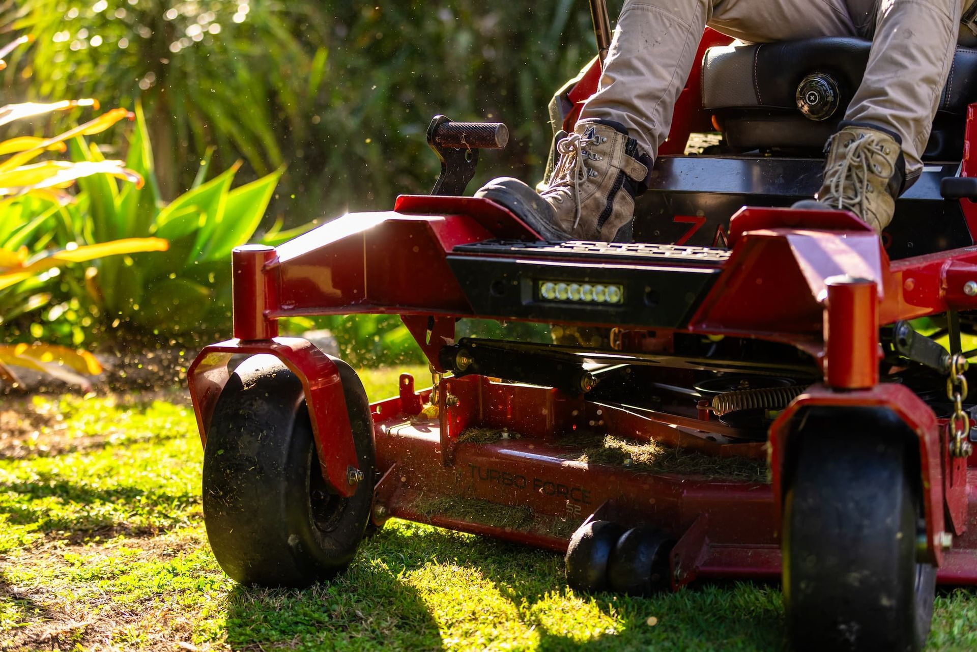 A person is riding a red zero turn lawn mower on a lush green lawn.
