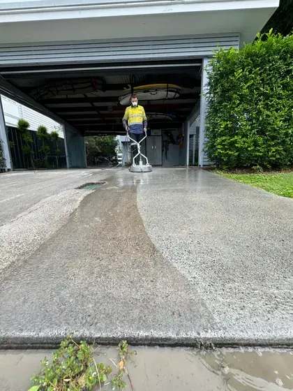 A man is cleaning a concrete driveway in front of a garage.