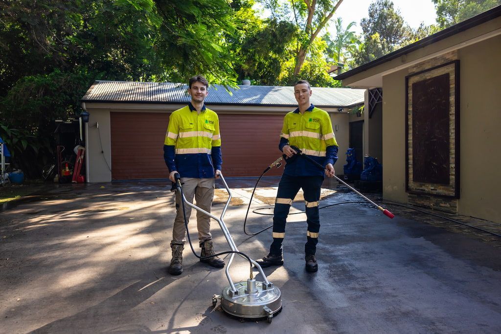 Two men are cleaning a driveway with a machine.