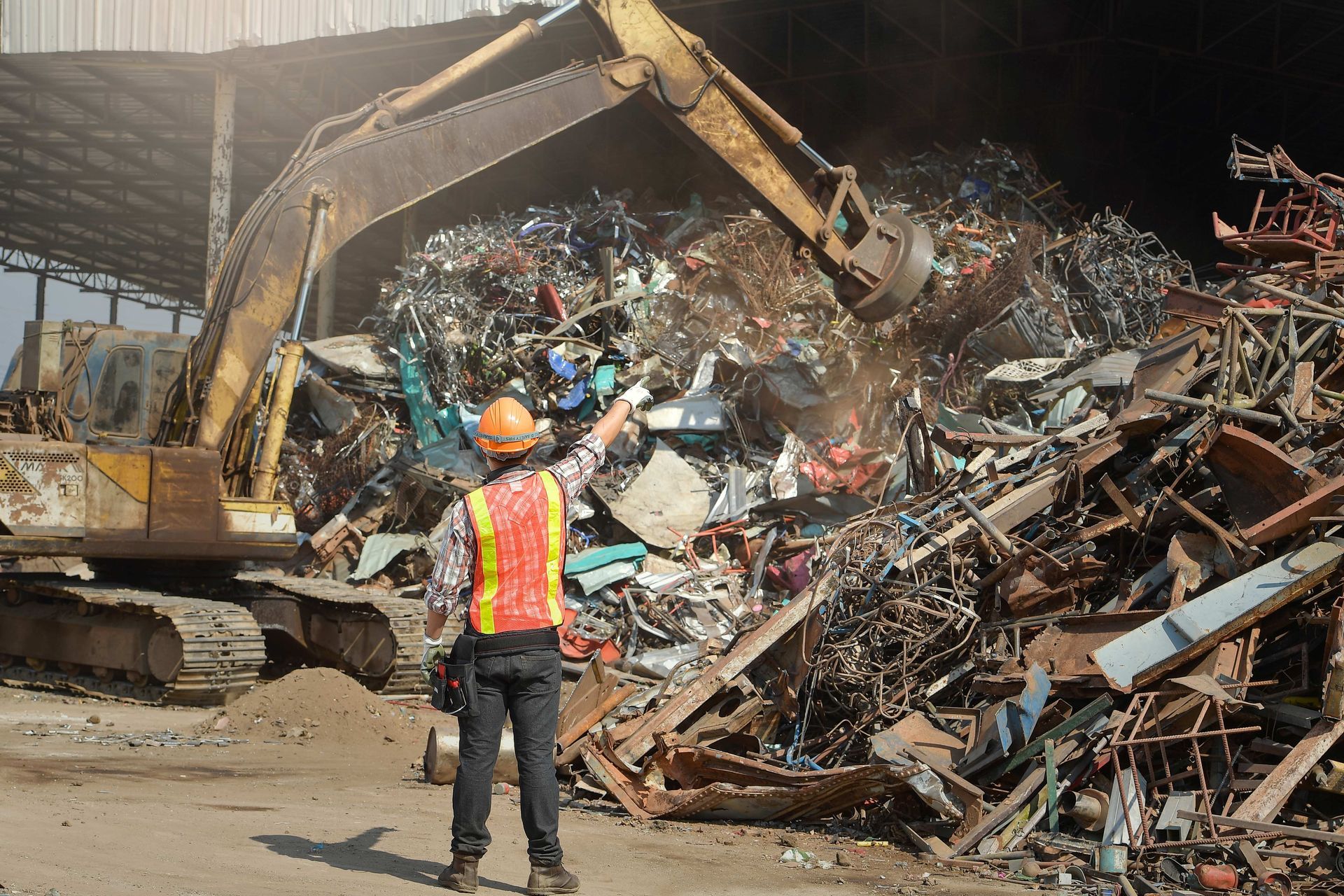 A recycling industry worker signaling to move the magnetic claw over a pile of scrap metal.
