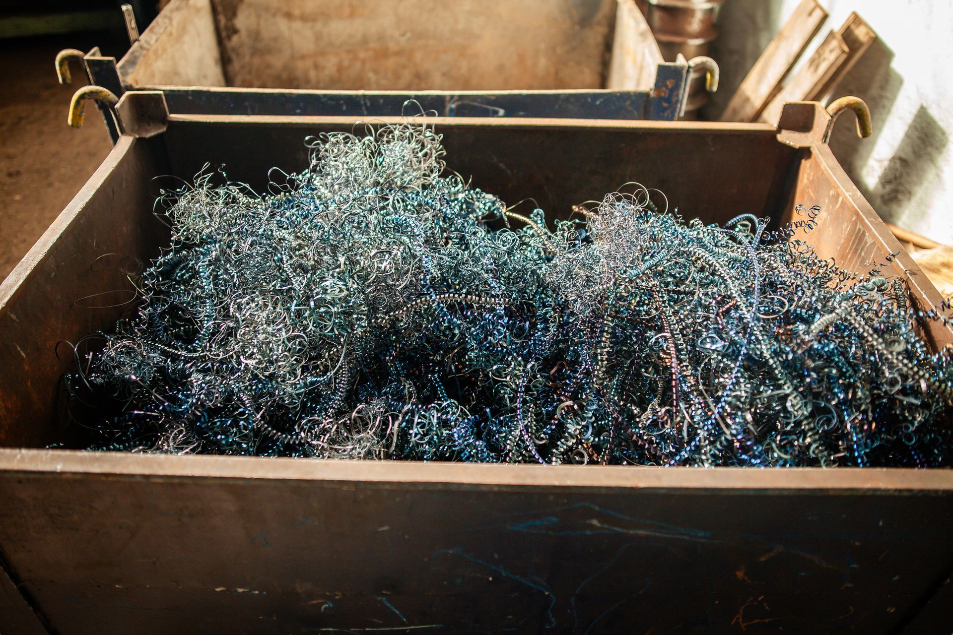 A bin filled with colourful metal shavings, ready for recycling in an industrial workshop.