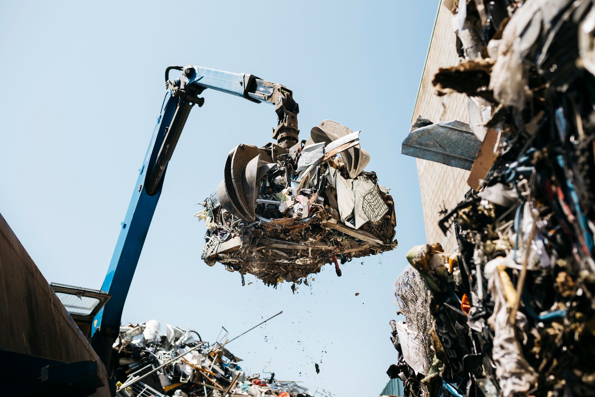 A hydraulic grabber lifts a rusty metal heap during scrap aluminum recycling at a scrapyard.