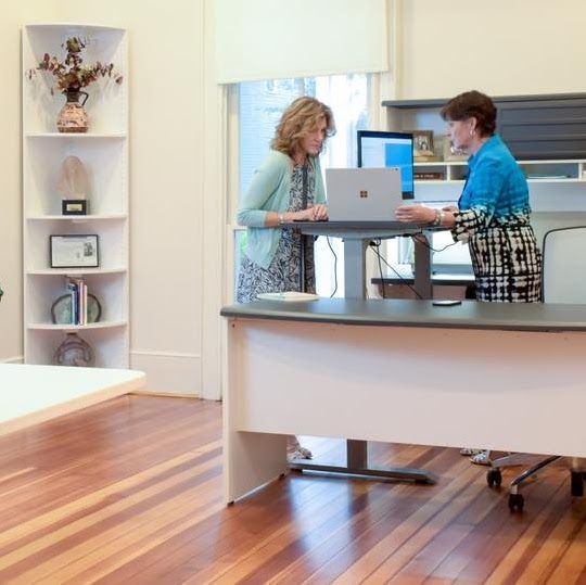 Two women are sitting at a desk with a laptop