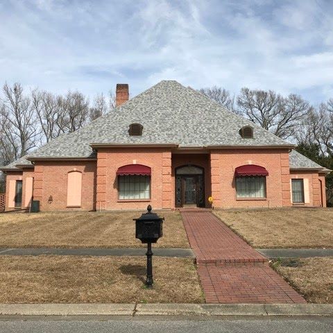 A large brick house with a gray roof and a mailbox in front of it.