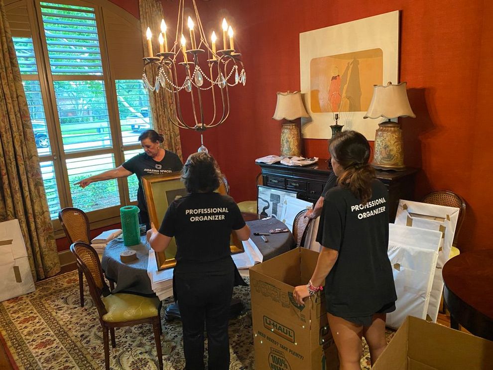 Amazing Spaces team moving boxes in a  room with chandelier, lamps, and a desk by the window.