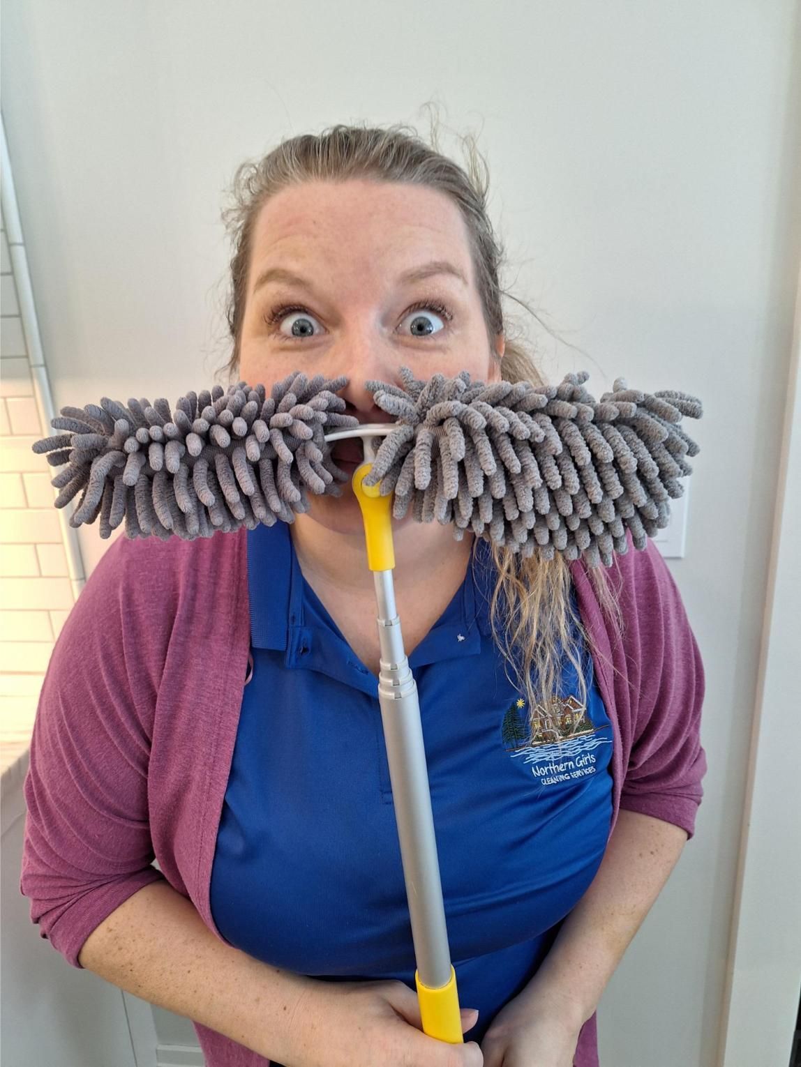 Woman with wide eyes, holding a gray duster to her face, making it look like a mustache.