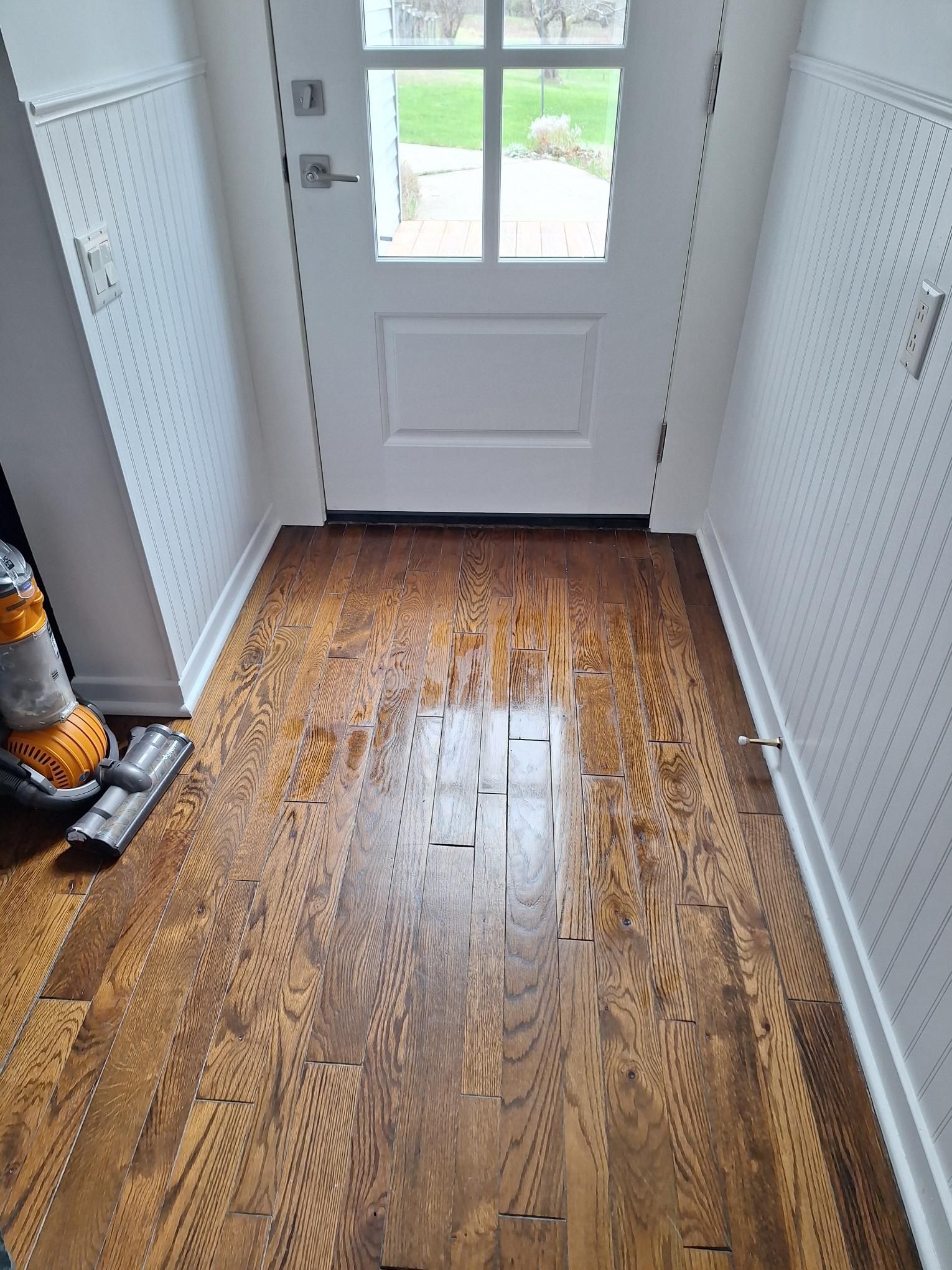 Entryway with hardwood floors, white door, pegboard walls, and vacuum cleaner.