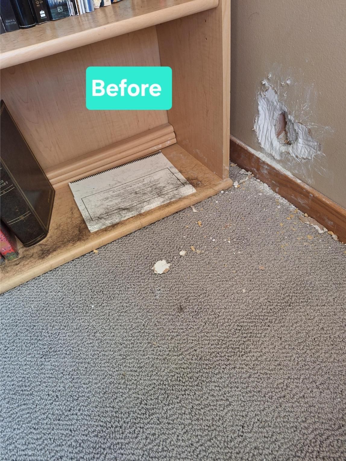 Damaged wall with hole and patch near bookshelf and carpet.