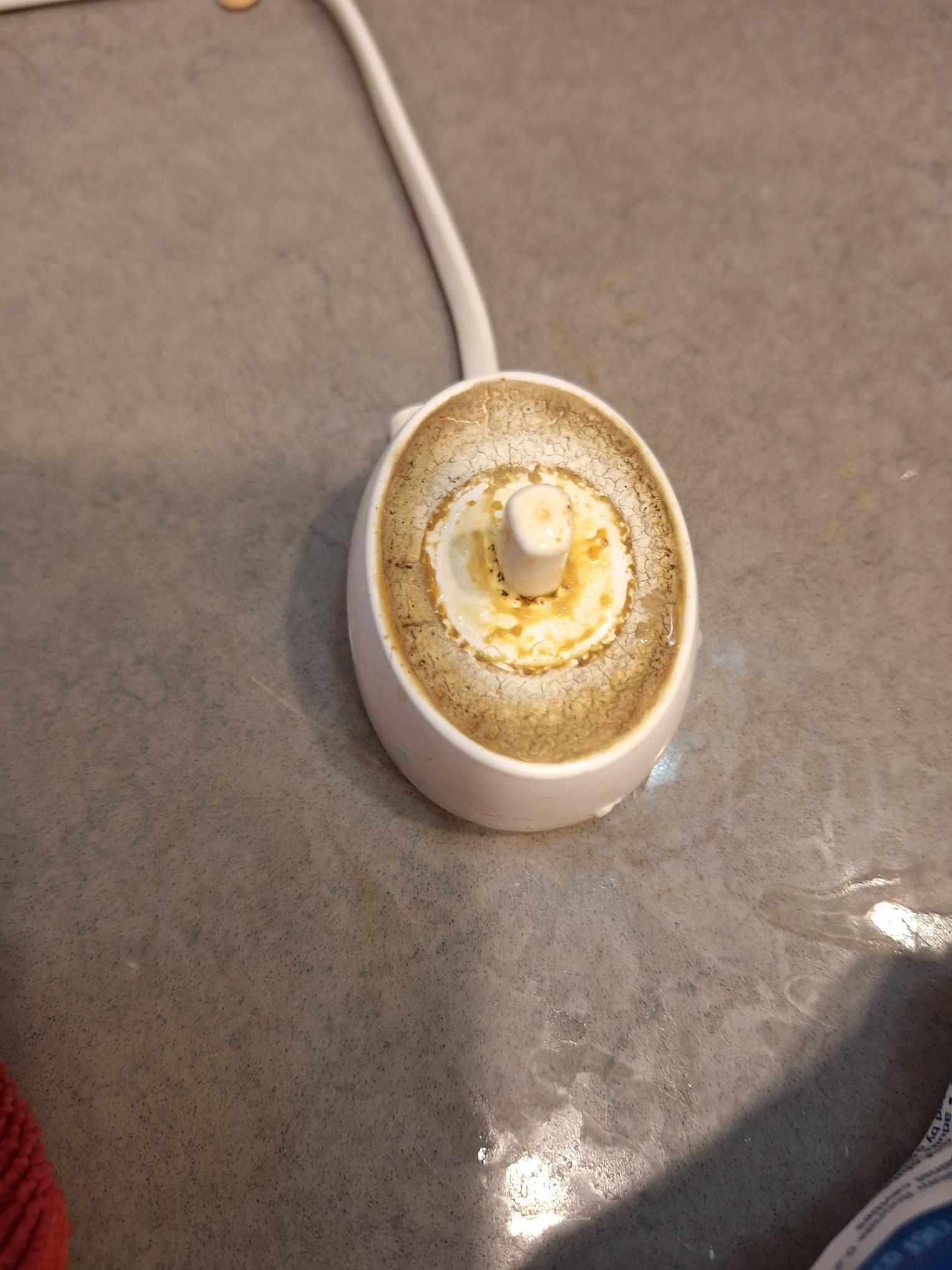 Dirty white electric toothbrush charger. Yellowish stains and grime visible on the top surface.