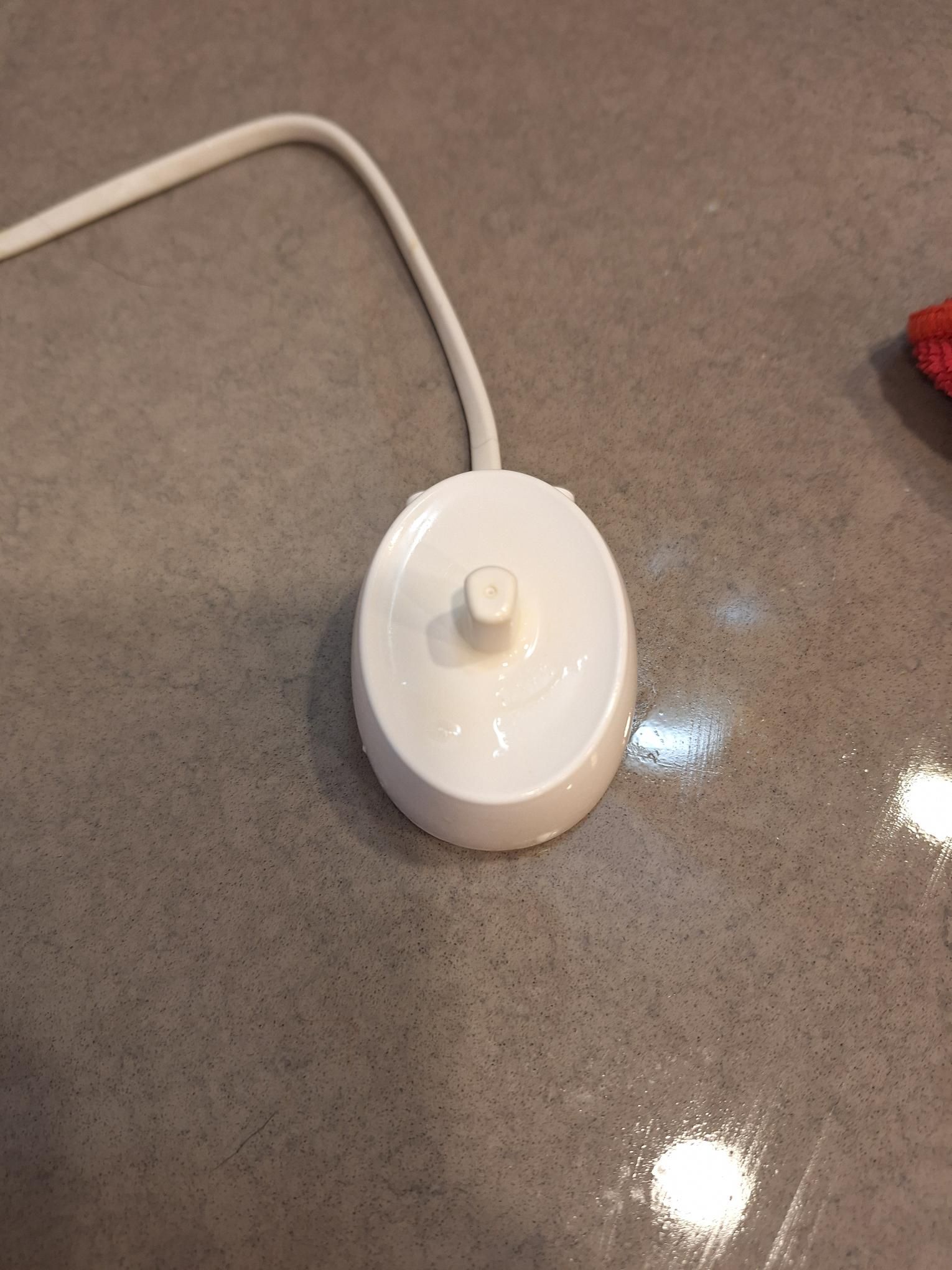 White electric toothbrush charging base with attached cord on a gray countertop.