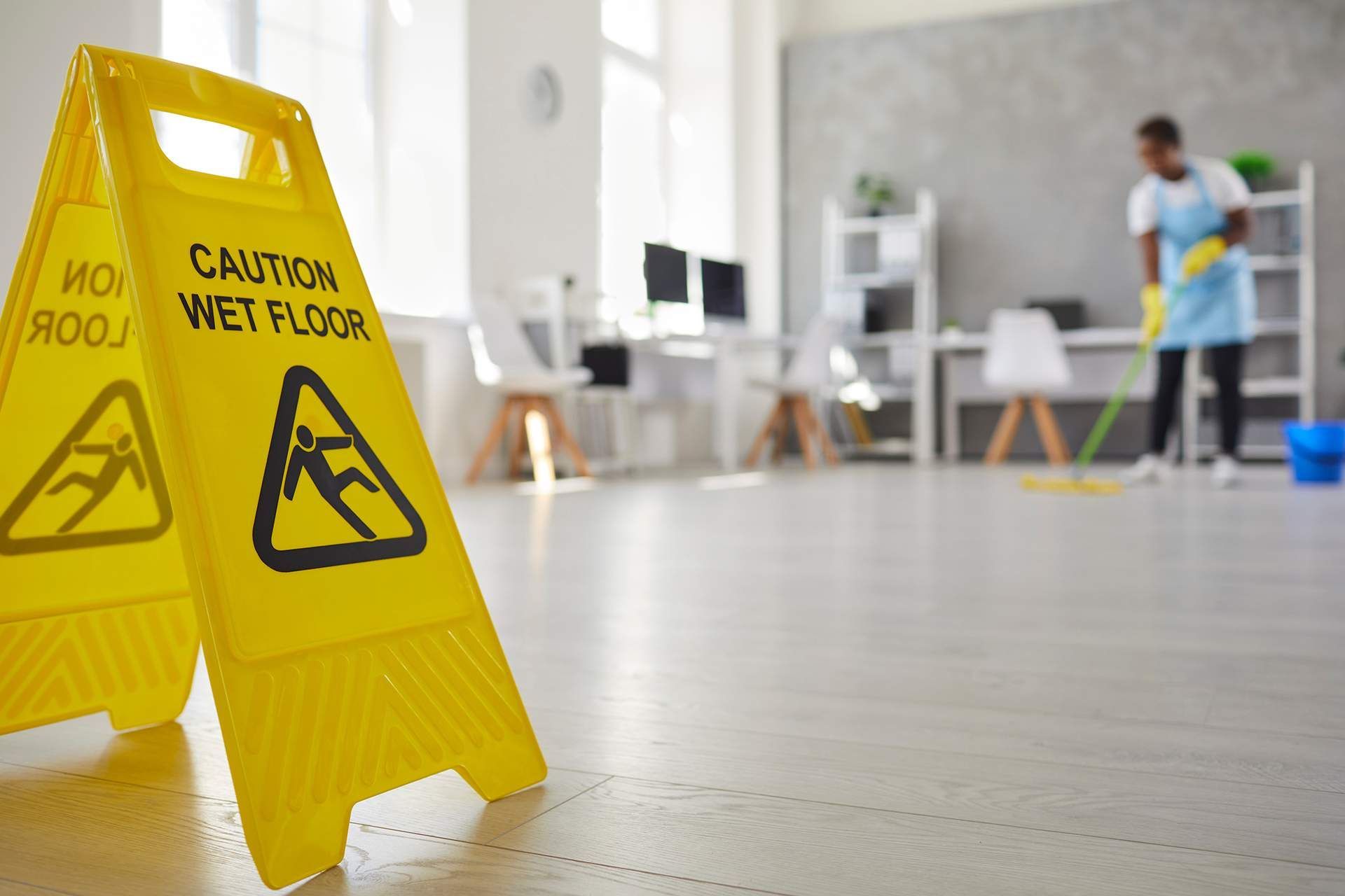 Yellow wet floor sign in an office; worker mopping floor.