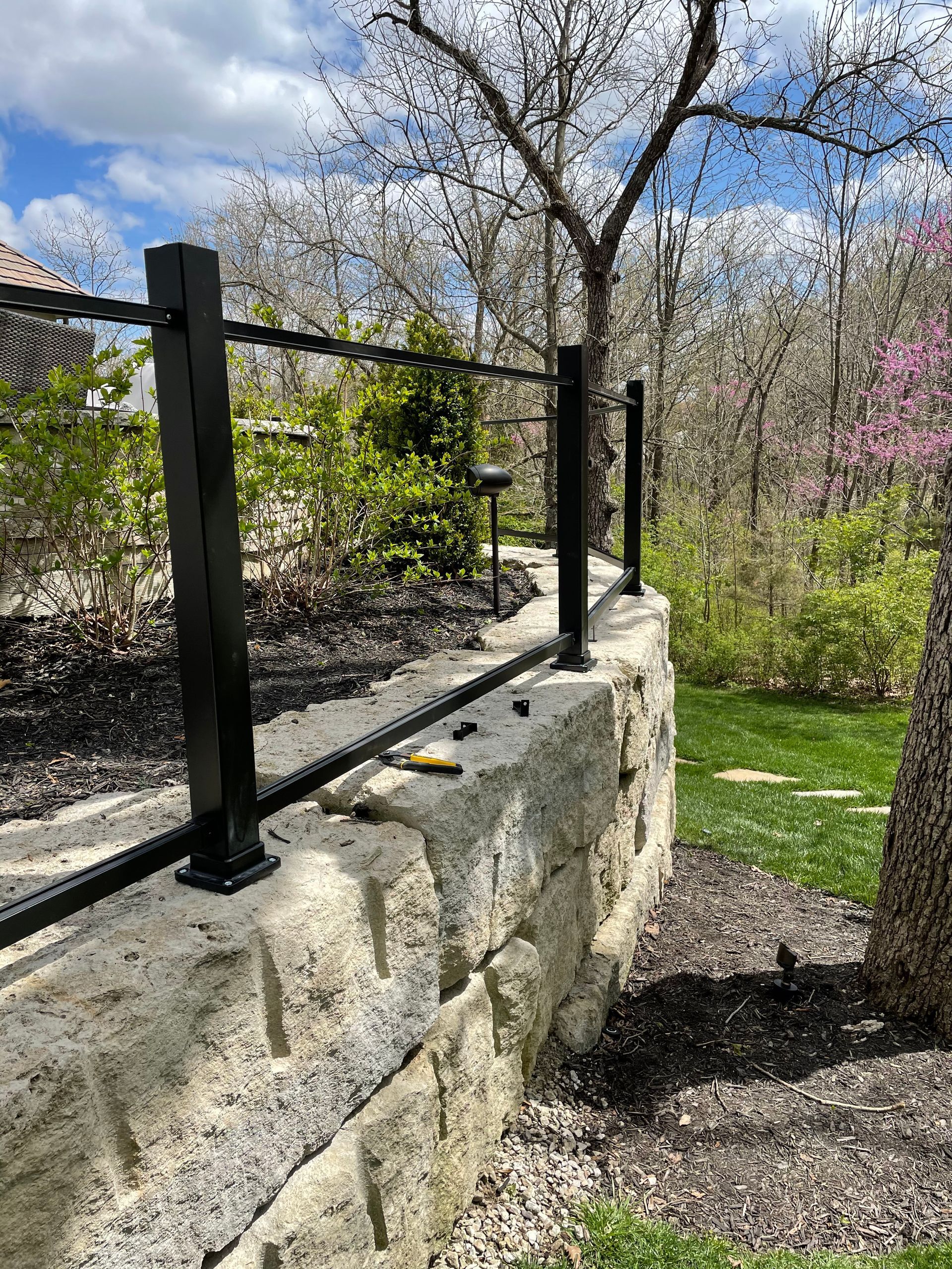 A black fence is sitting on top of a stone wall in a garden.
