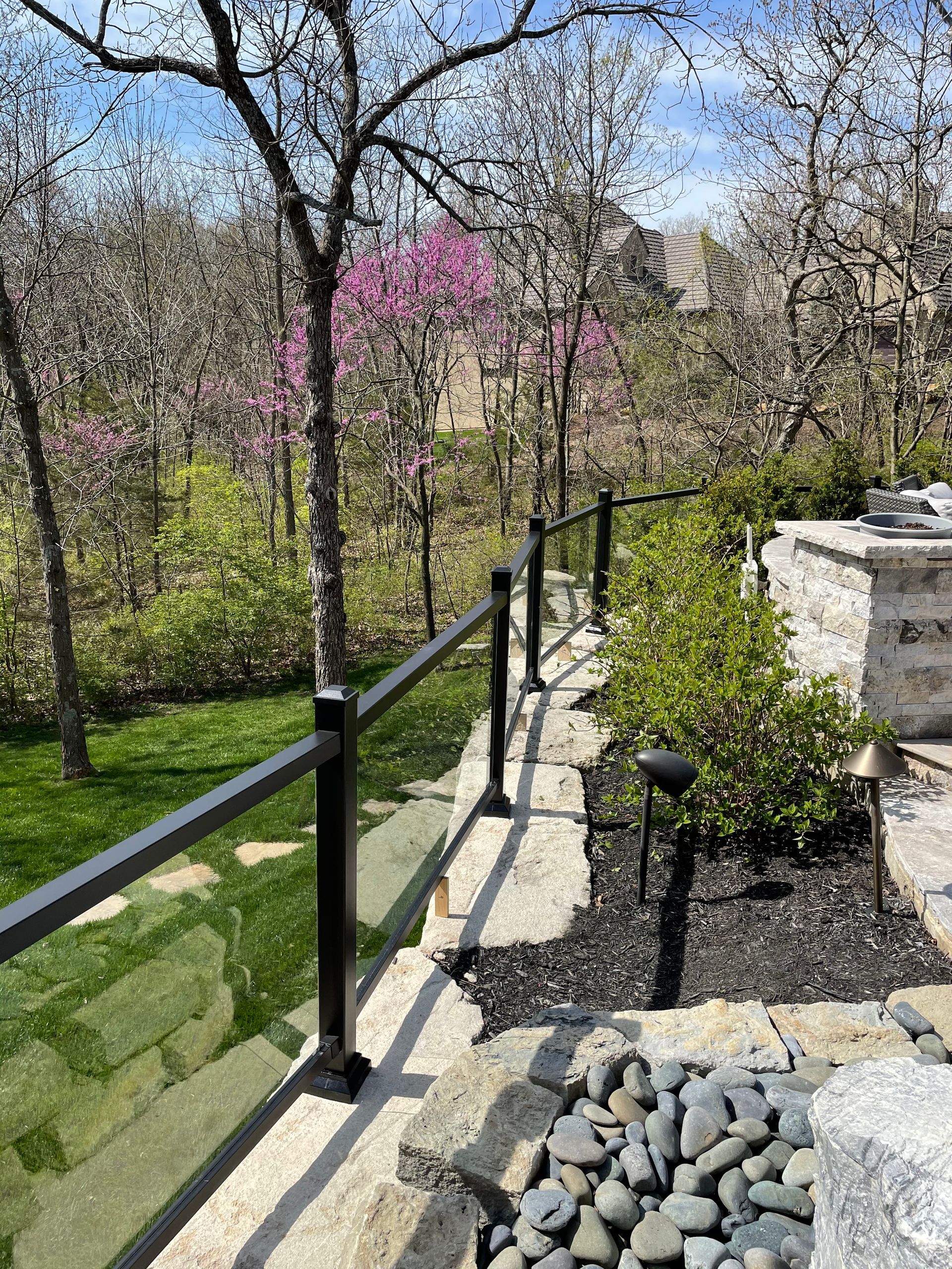 A glass railing surrounds a lush green yard with trees and rocks.