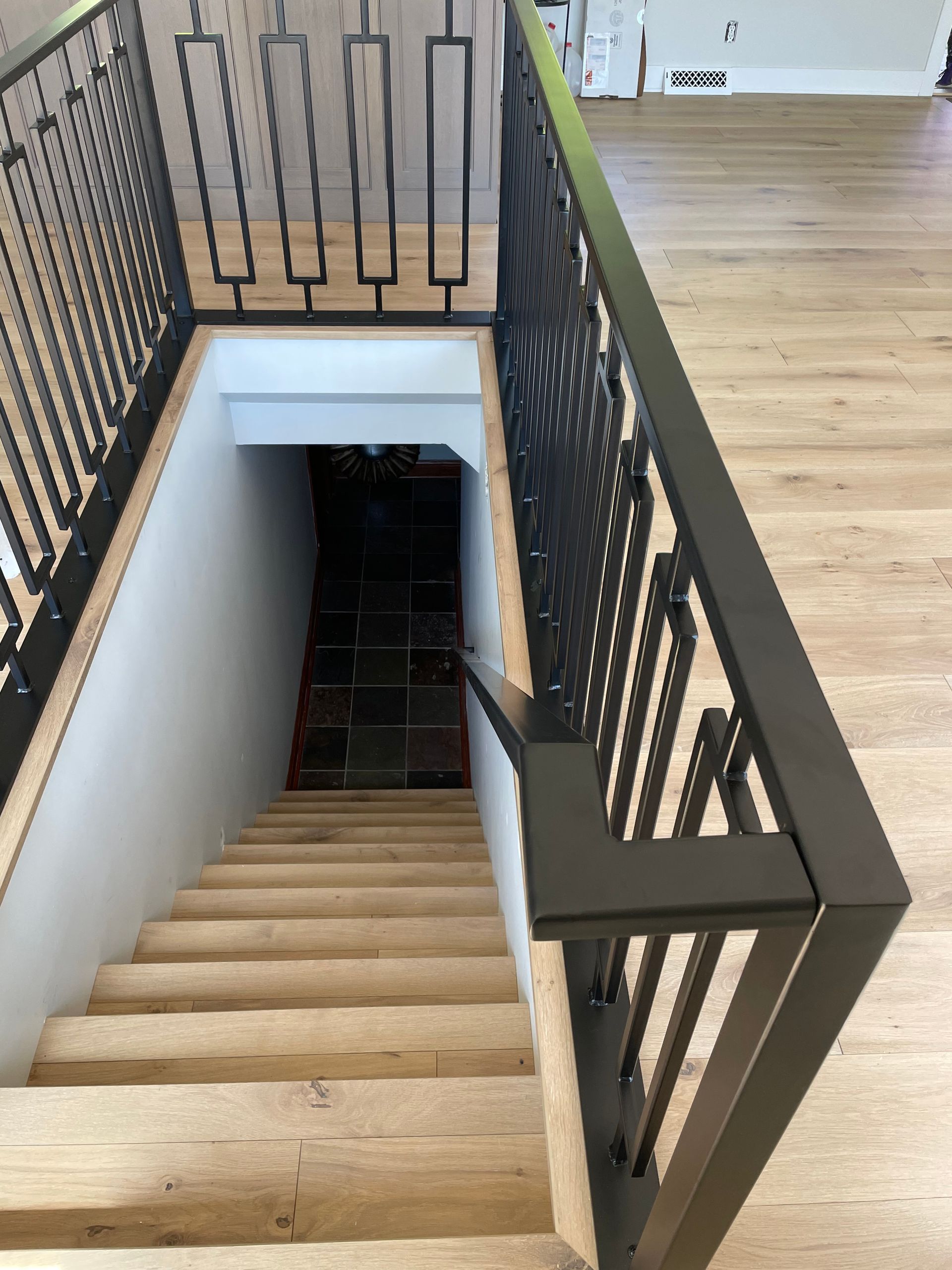 A wooden staircase with a black railing leading to a basement.