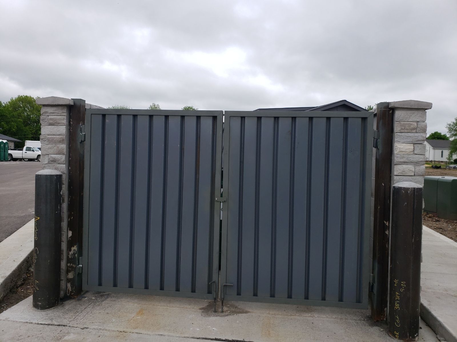A gray trash  gate is sitting on a sidewalk next to a brick wall.