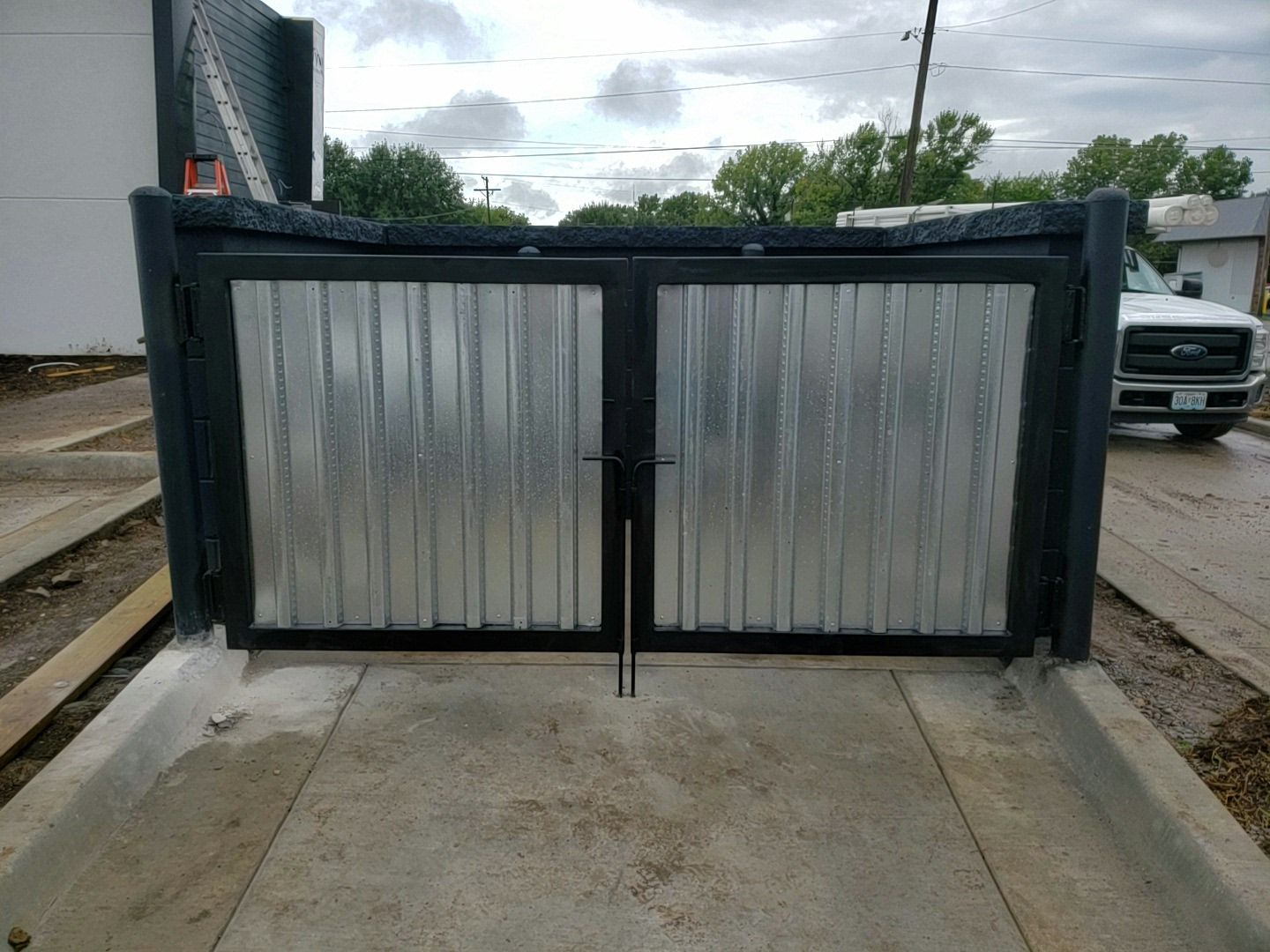 A metal trash gate is sitting on the side of the road next to a truck.