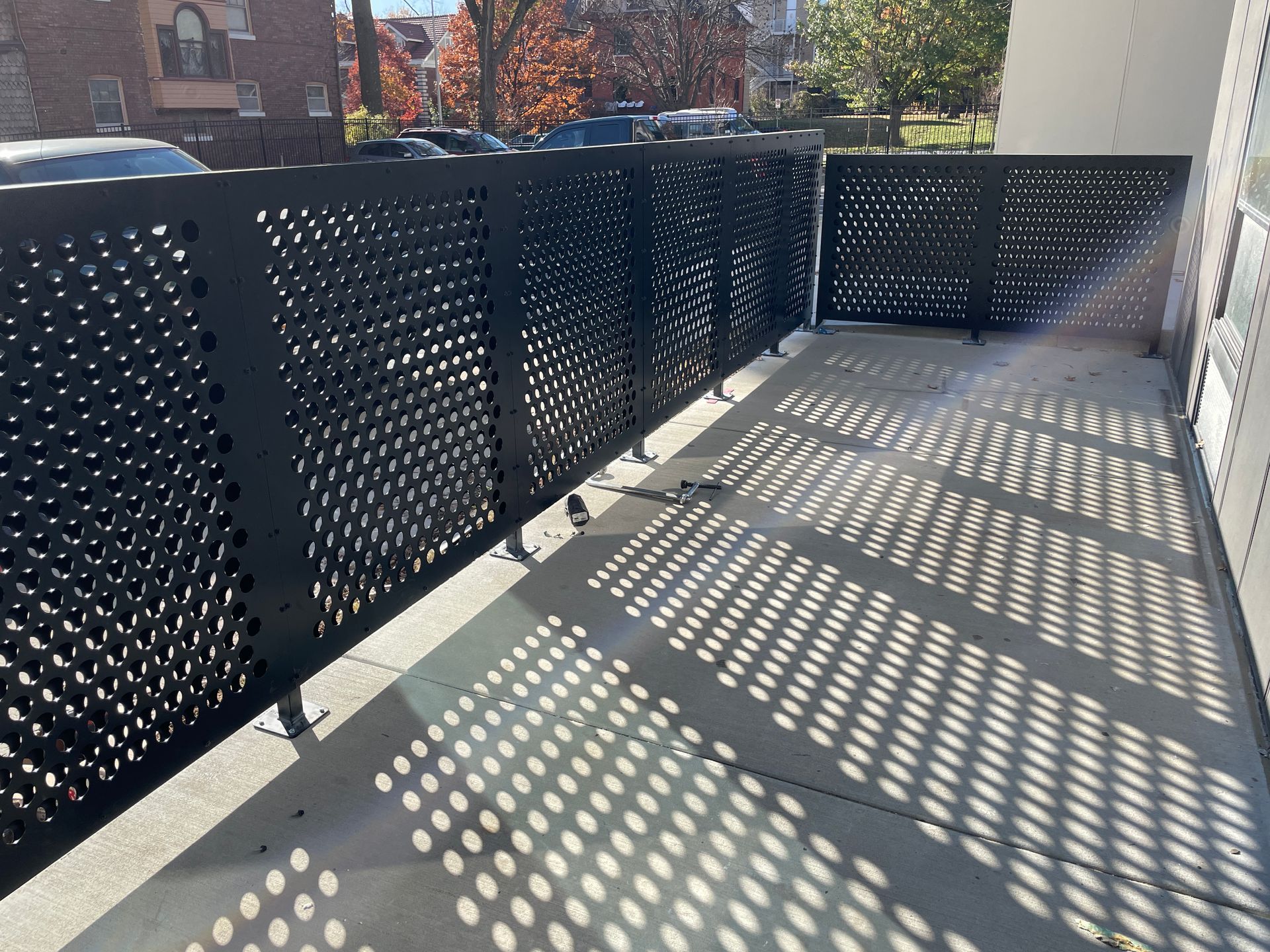 A balcony with a black metal fence and shadows on the ground.