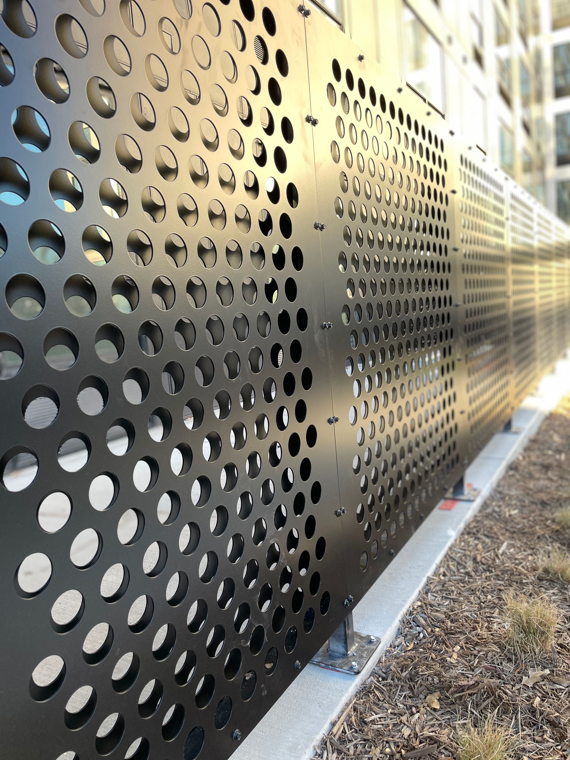 A black metal fence with holes in it is sitting next to a building.