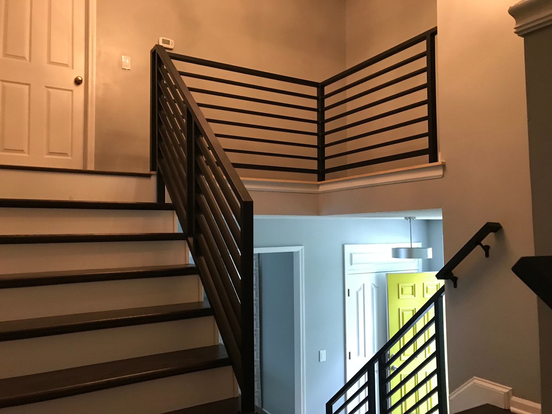 A staircase in a house with a metal railing and a yellow door.