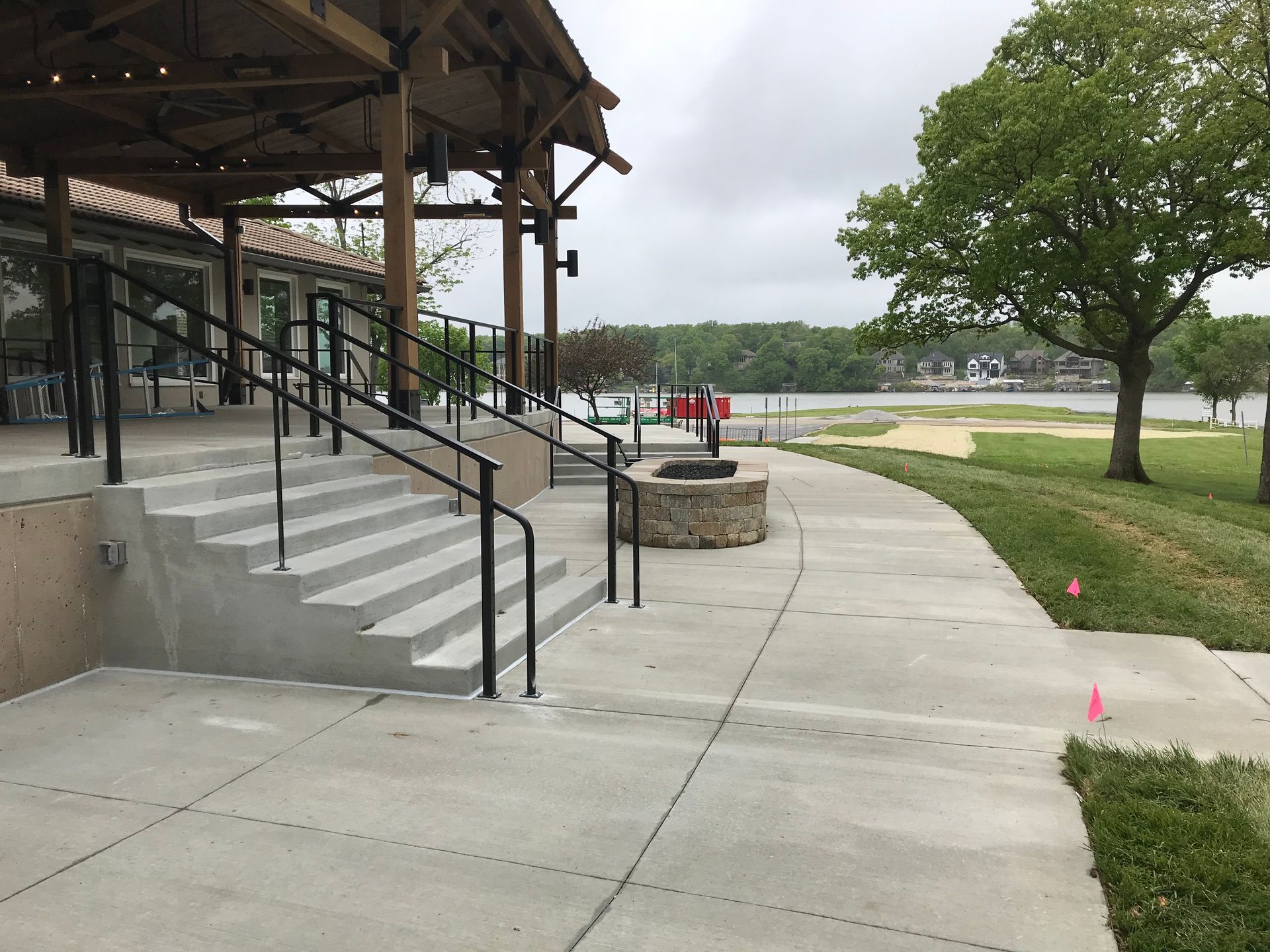 A concrete walkway with black railings and stairs and a fire pit in the background 