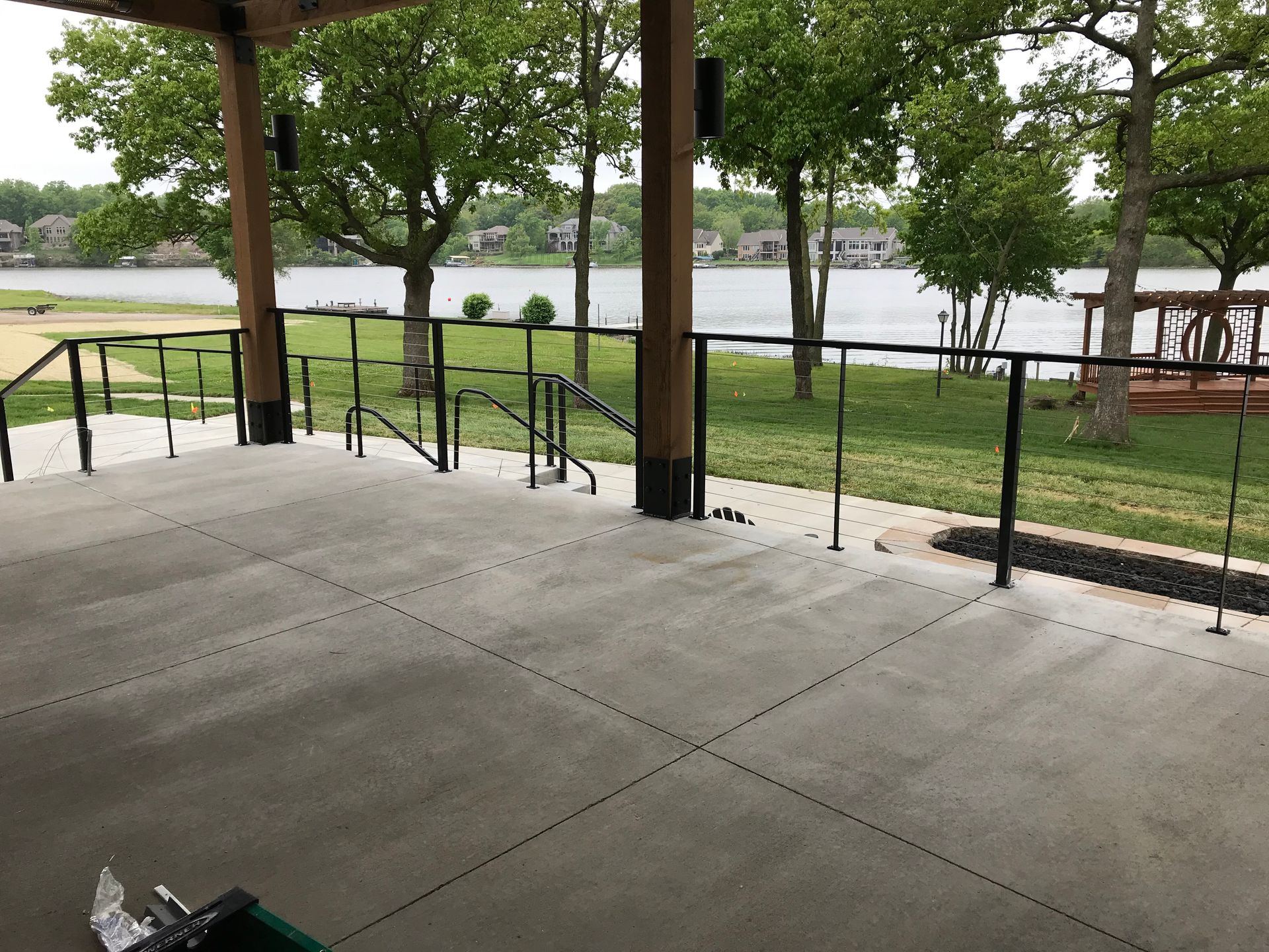 A concrete deck with stairs leading up to a lake with black railing