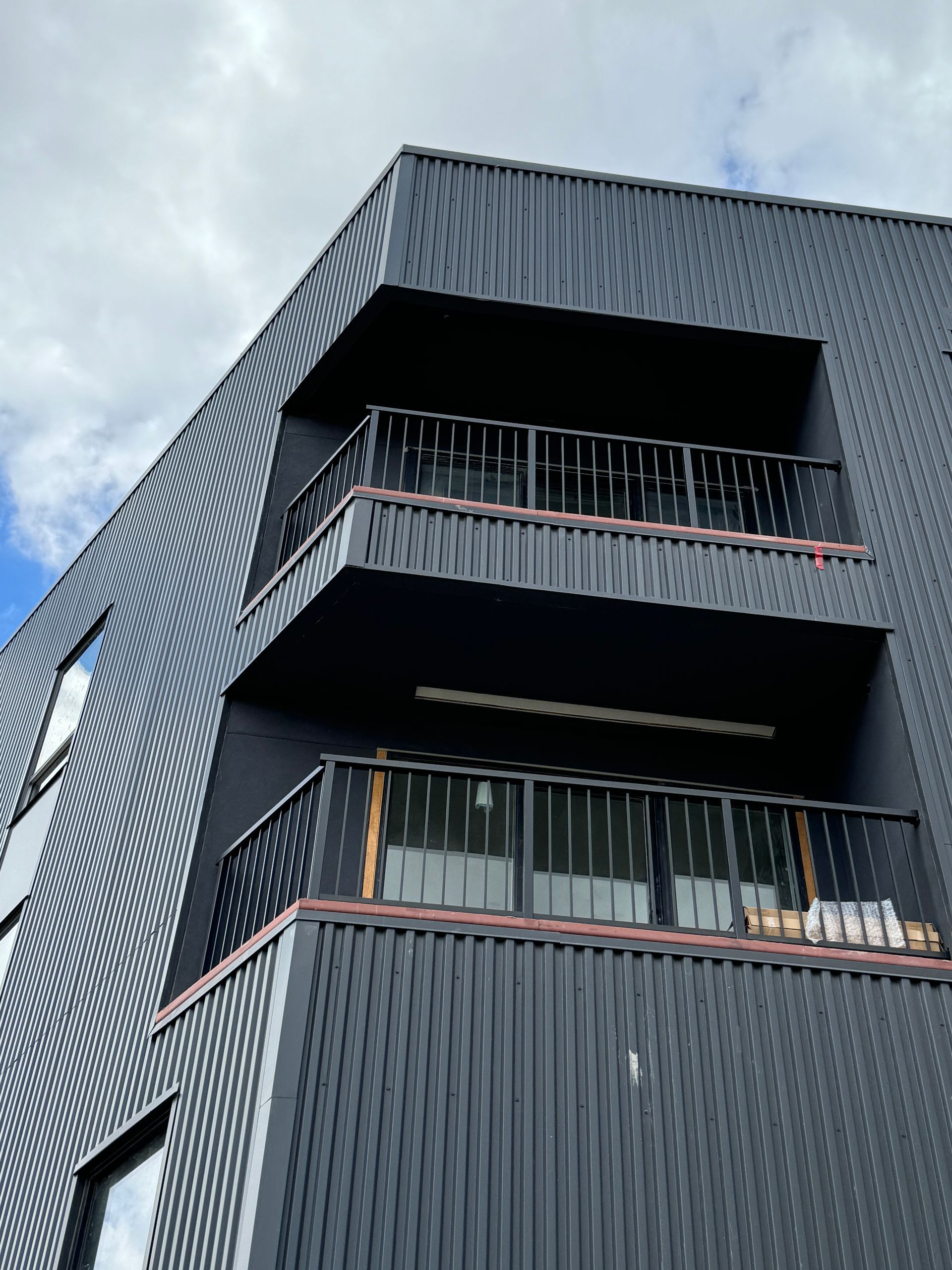 A black building with balconies, black handrails and a blue sky in the background