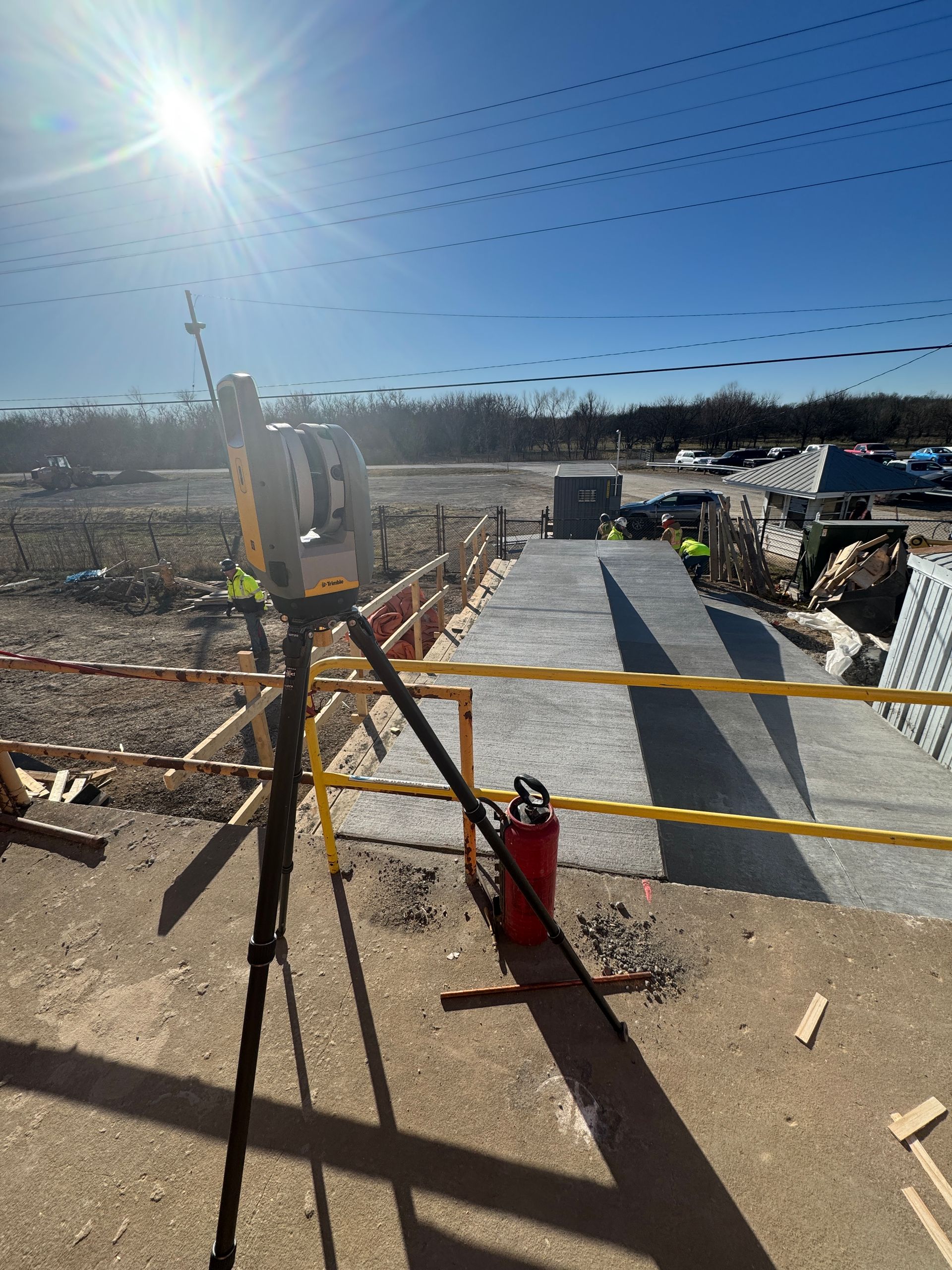 A person is standing in front of a construction site with a camera on a tripod.