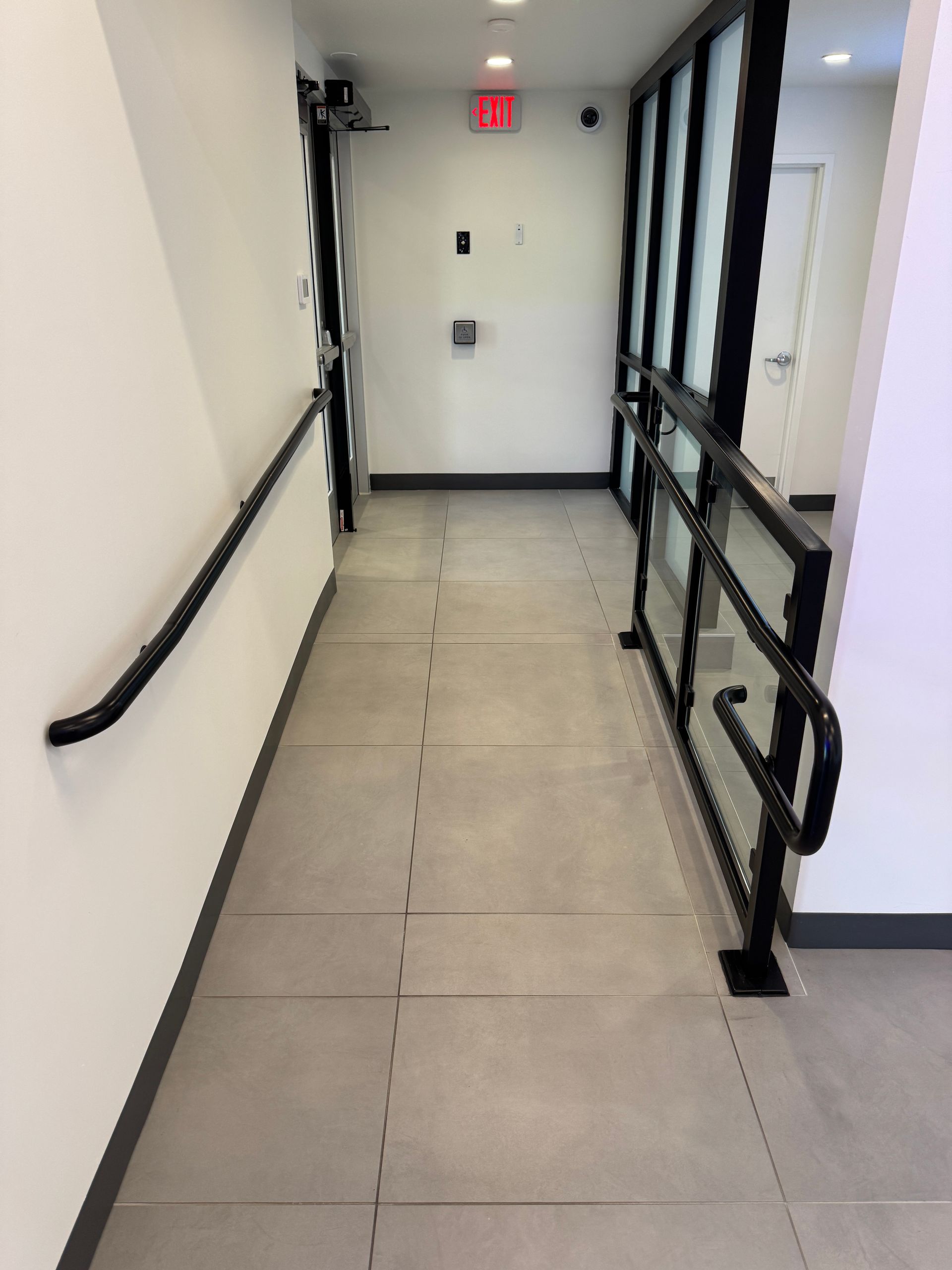 A long hallway with a red exit sign on the wall with aluminum handrail