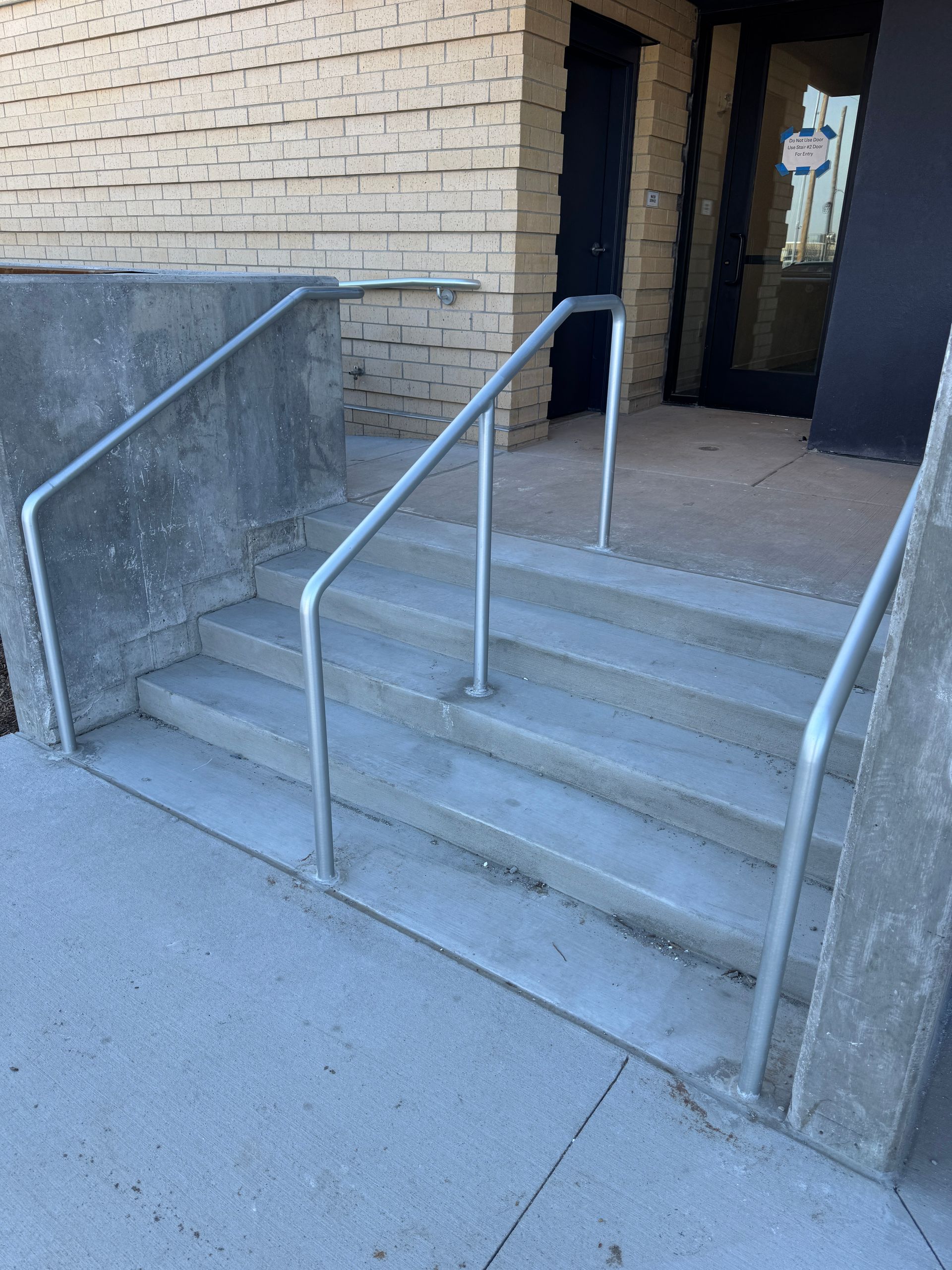 A set of stairs with a metal railing and a brick building in the background