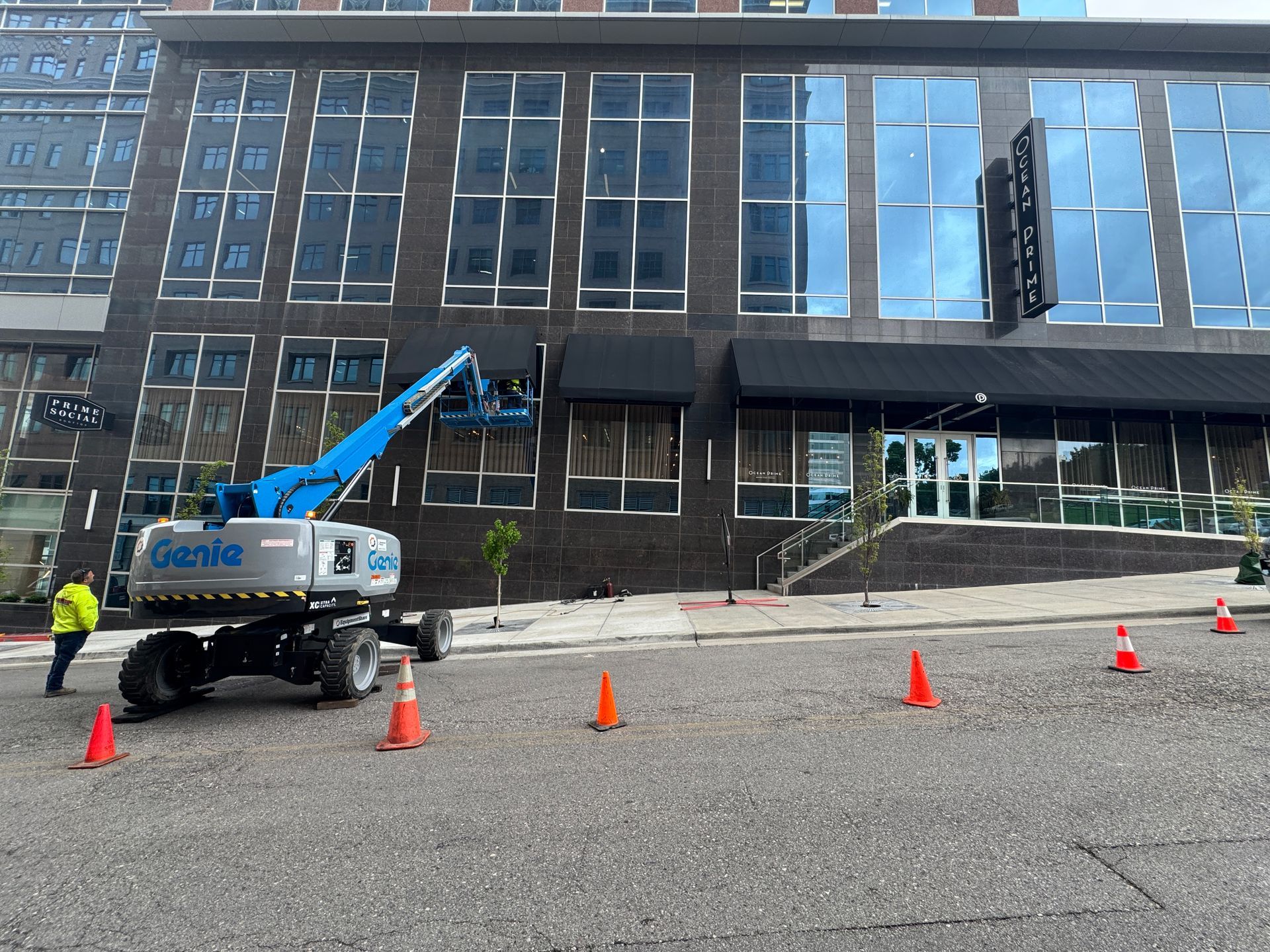 A genie lift is parked in front of a large building installing a custom awning