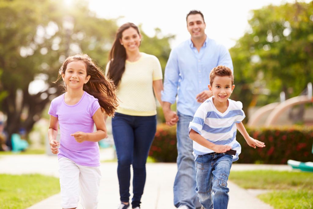 A family is walking down a path in a park holding hands.