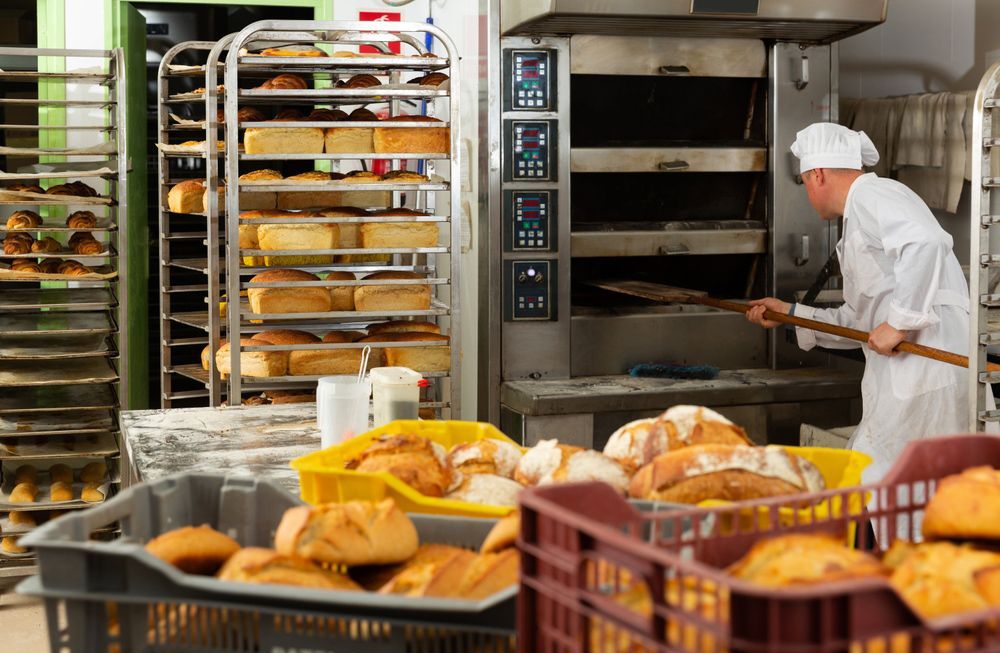 A baker is putting bread into an oven in a bakery.