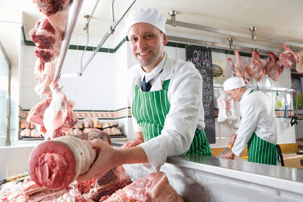 A man is holding a piece of meat in a butcher shop.