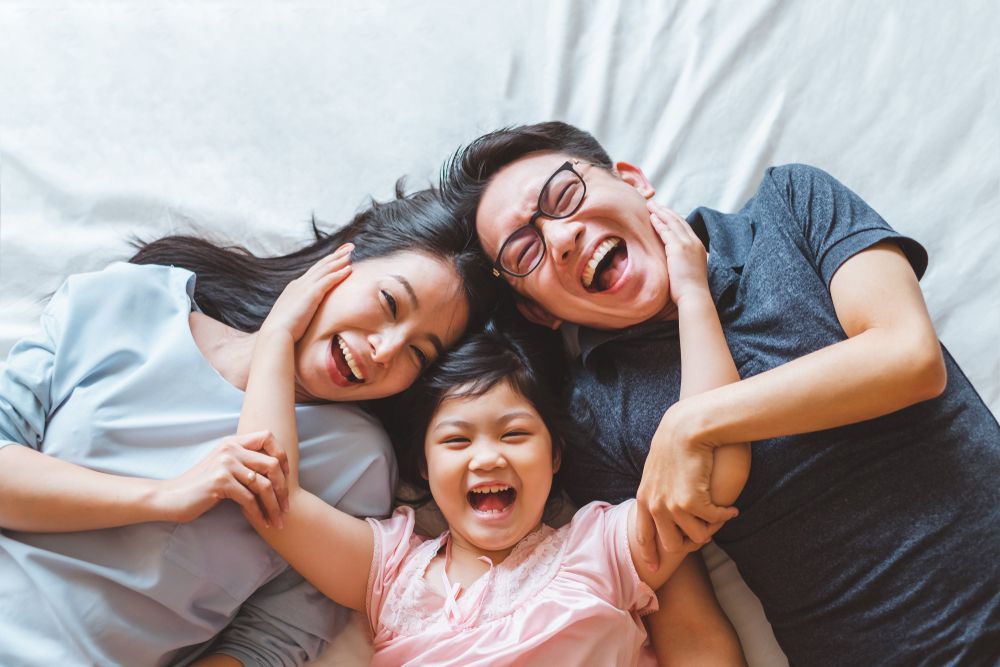 A family is laying on a bed together and laughing.