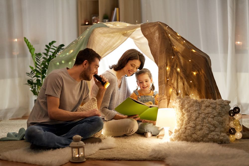 A family is sitting in a tent reading a book.