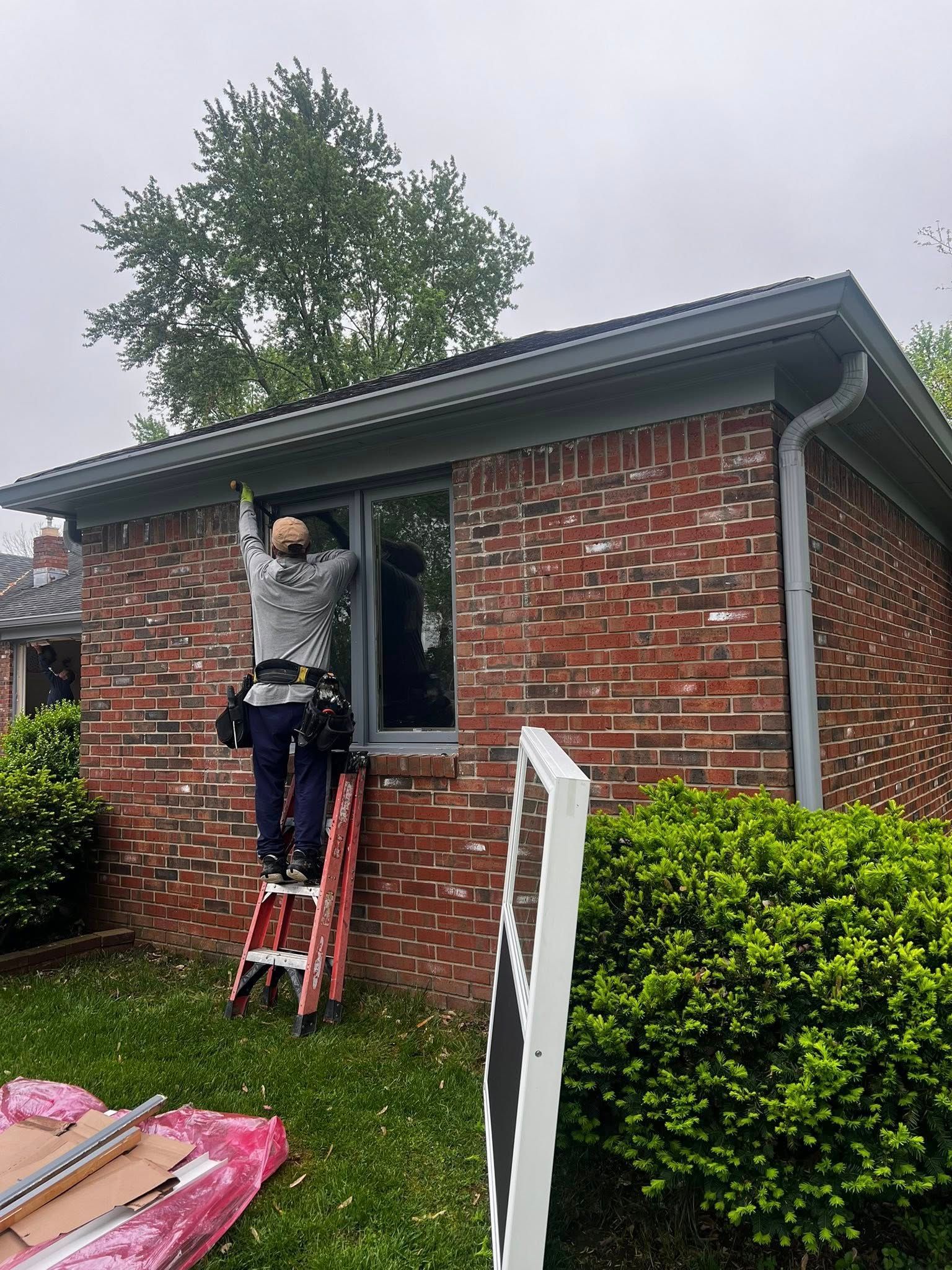 A man is standing on a ladder in front of a brick house.