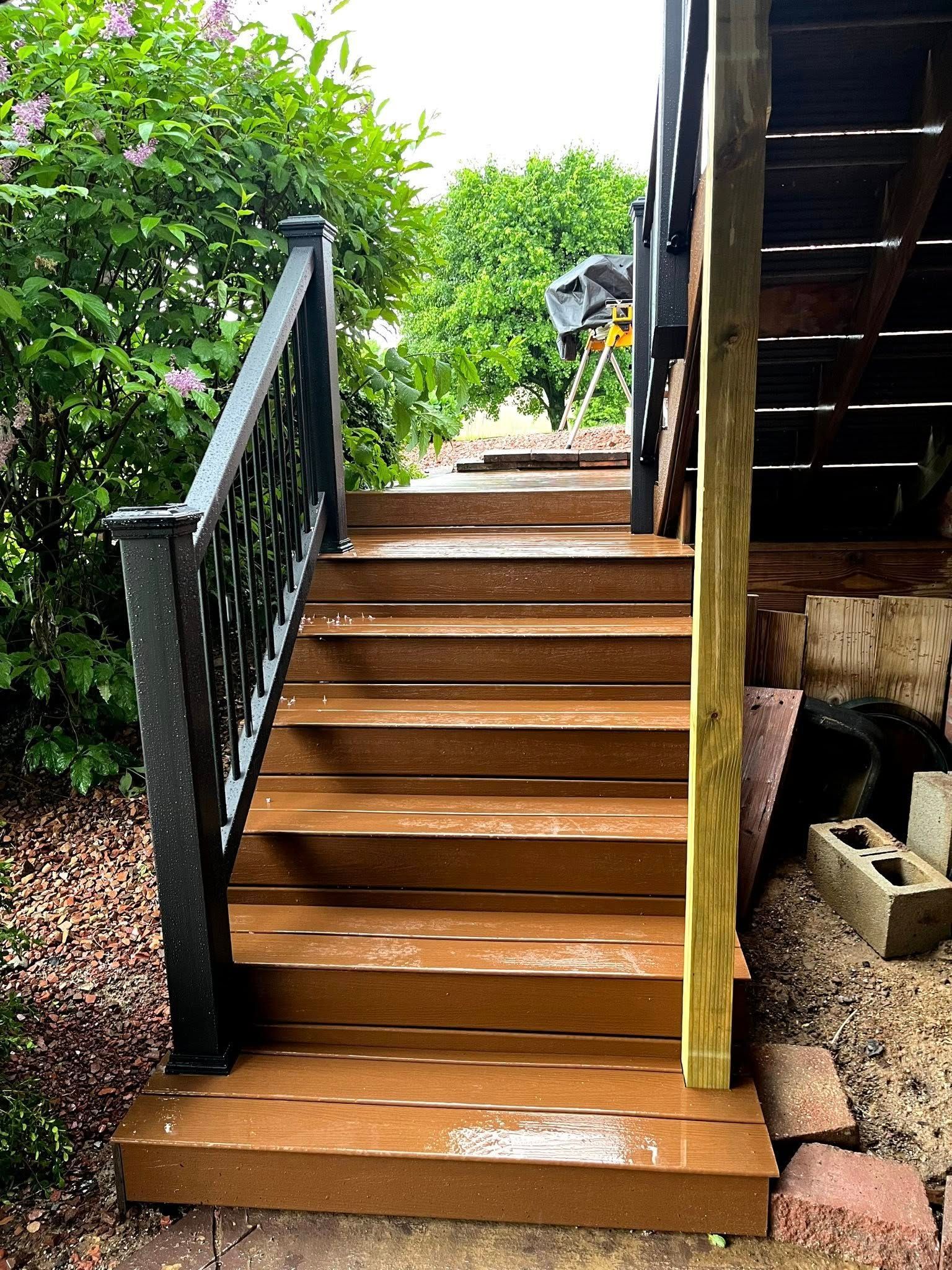 A set of wooden stairs leading up to a deck with a black railing.