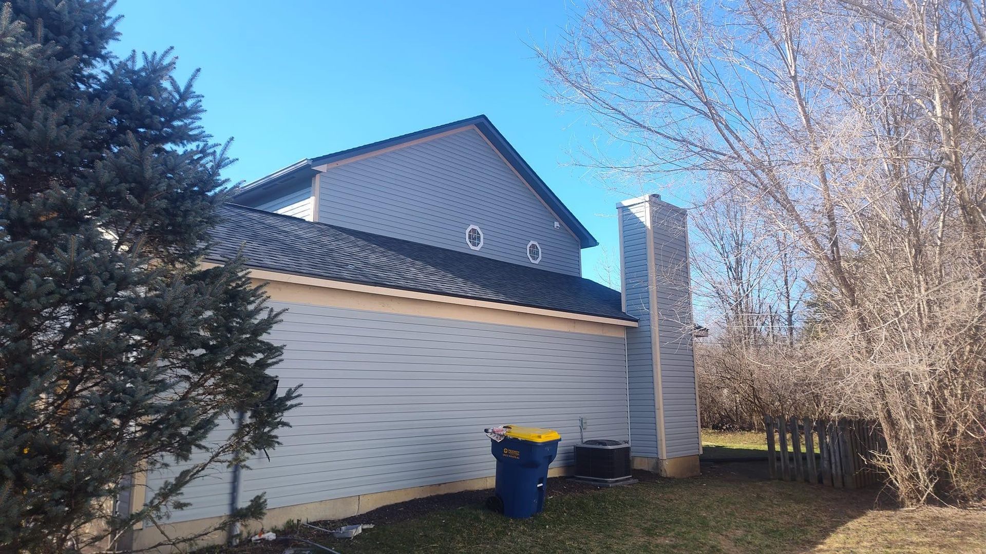 A white house with a blue trash can in front of it.