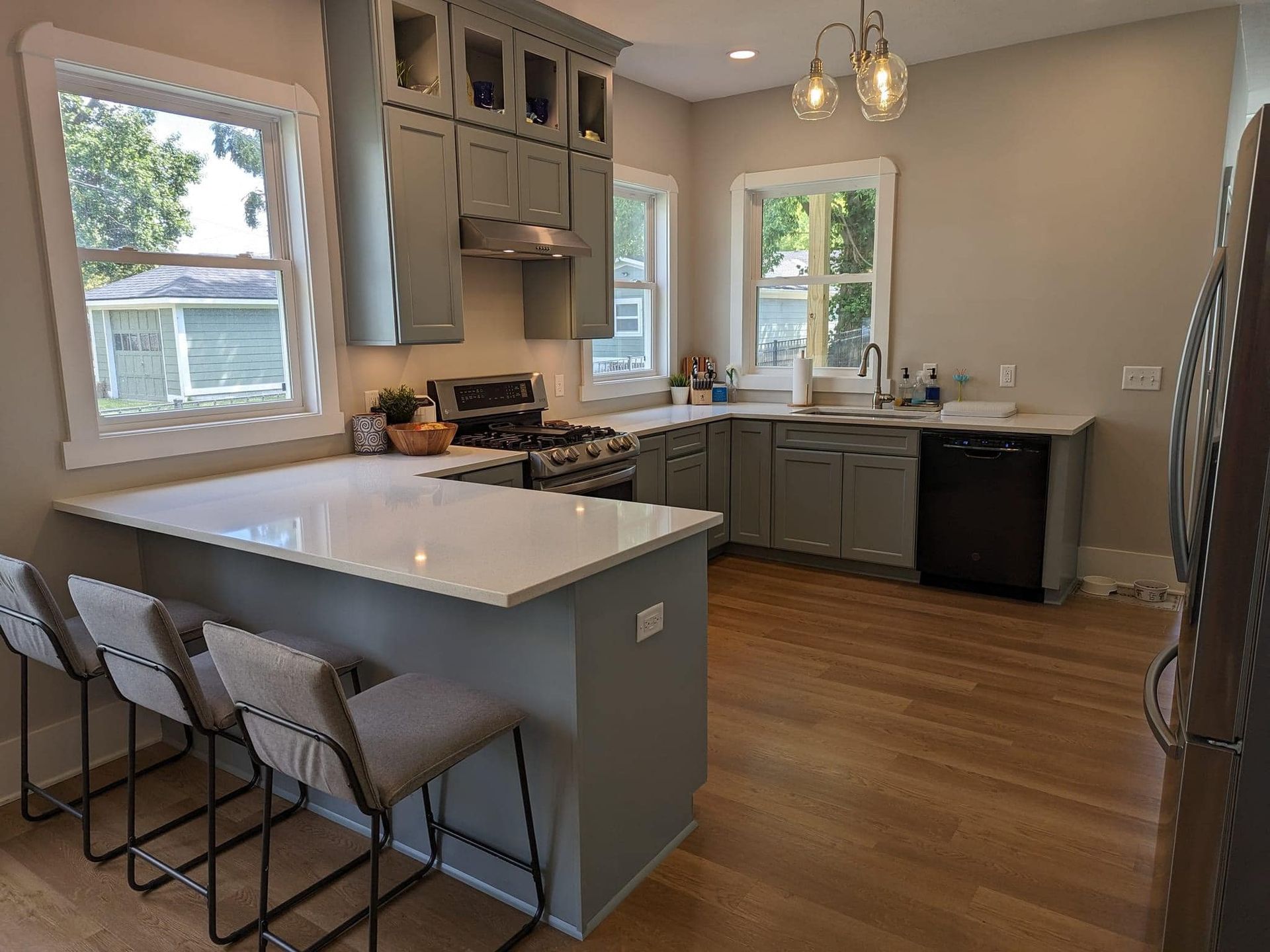 A kitchen with gray cabinets , white counter tops , a stove , a sink , and a dishwasher.