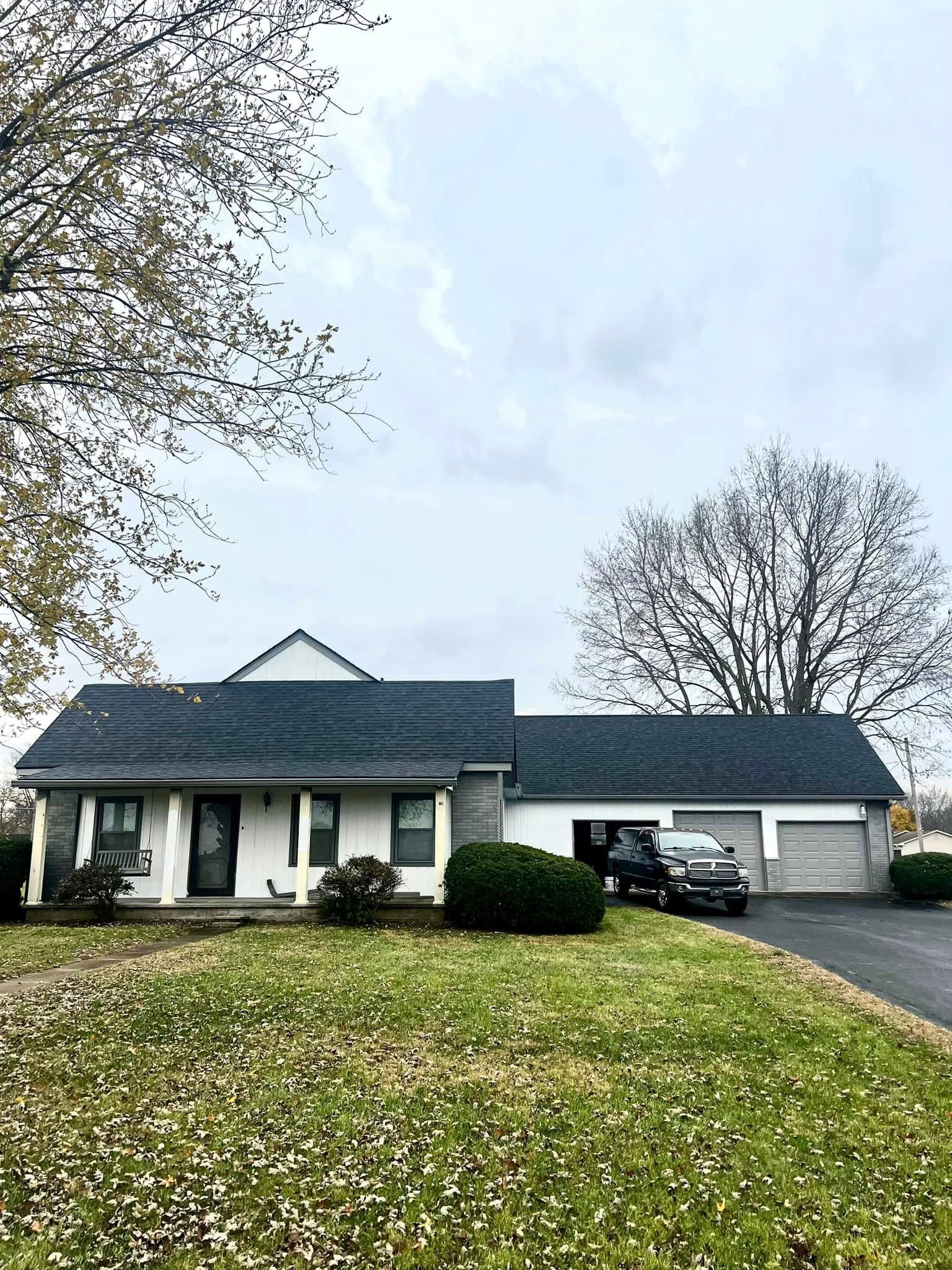 A white house with a black roof and a car parked in front of it.