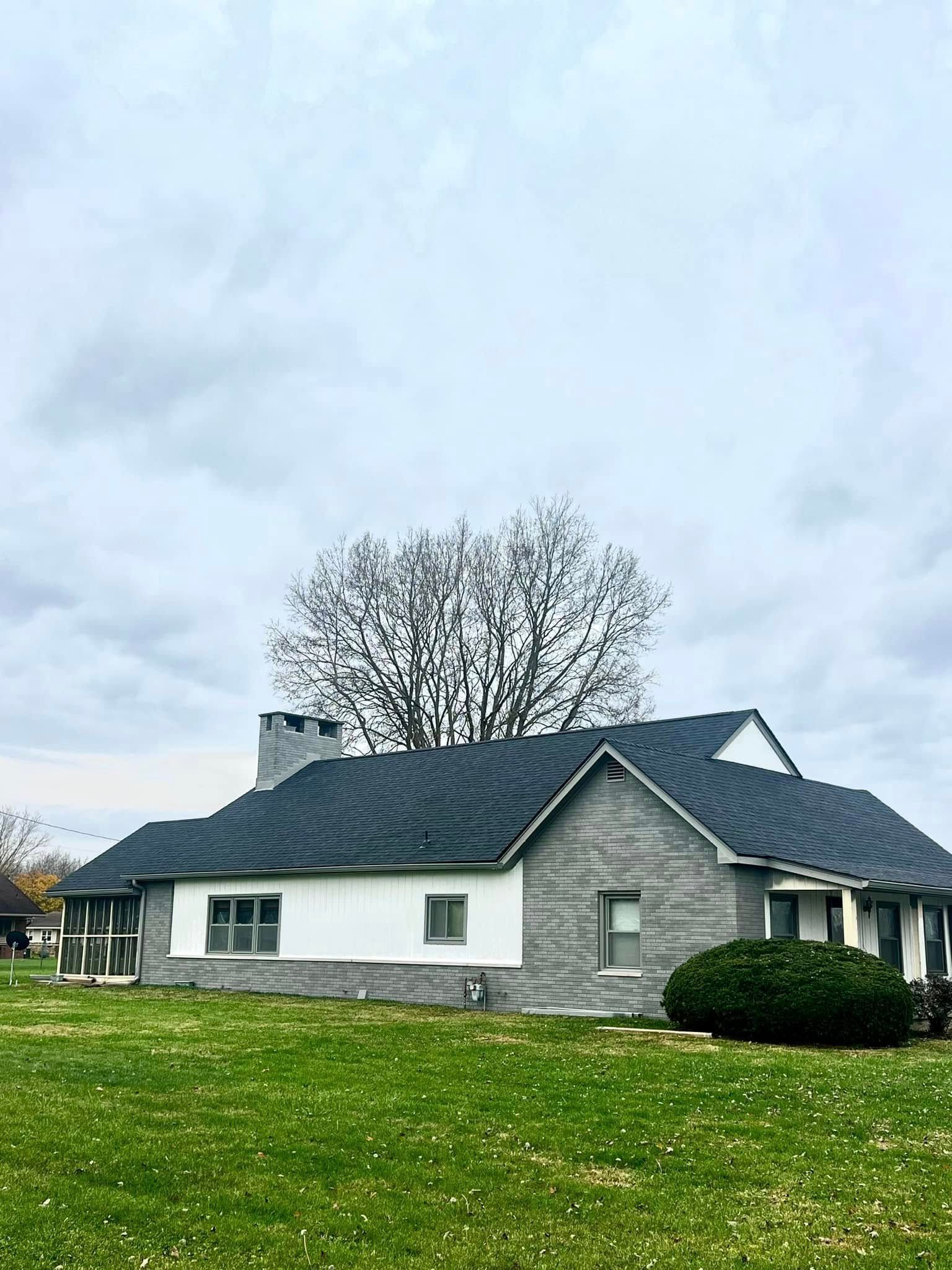 A white house with a black roof is sitting on top of a lush green field.