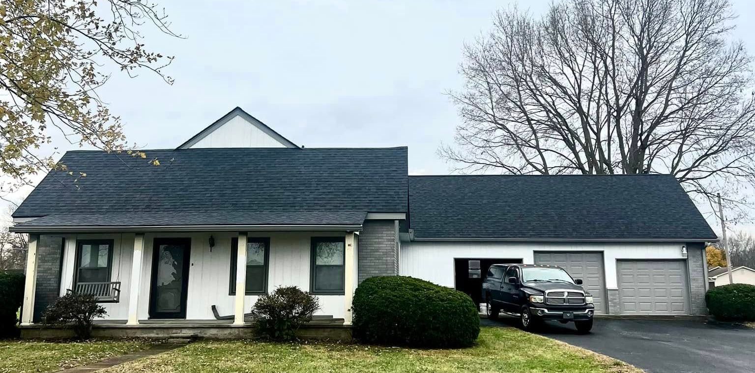 A white house with a black roof and a truck parked in front of it.